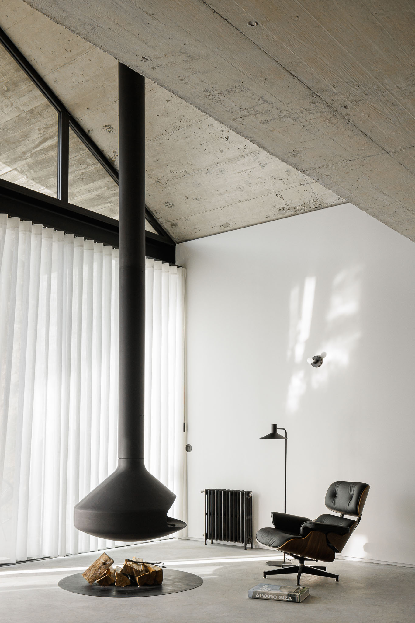 Casa NaMora: Sala de estar com lareira suspensa, poltrona de design e teto em betão aparente com vigas metálicas. — Casa NaMora arquitetura David Bilo Arquitectos e Filipe Pina Arquitectura em Guarda