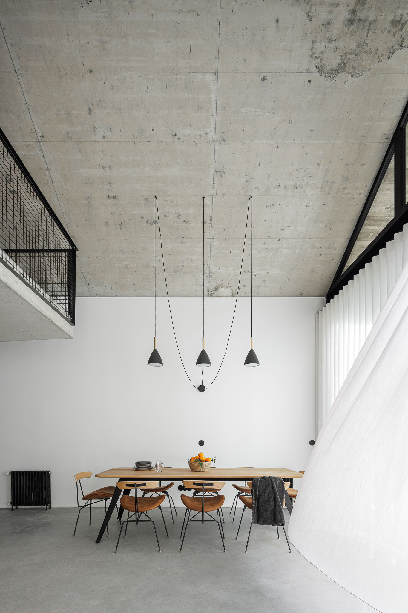Casa NaMora: Sala de jantar com mesa de madeira, cadeiras de design e vista para o mezanino, sob teto em betão. — Casa NaMora arquitetura David Bilo Arquitectos e Filipe Pina Arquitectura em Guarda