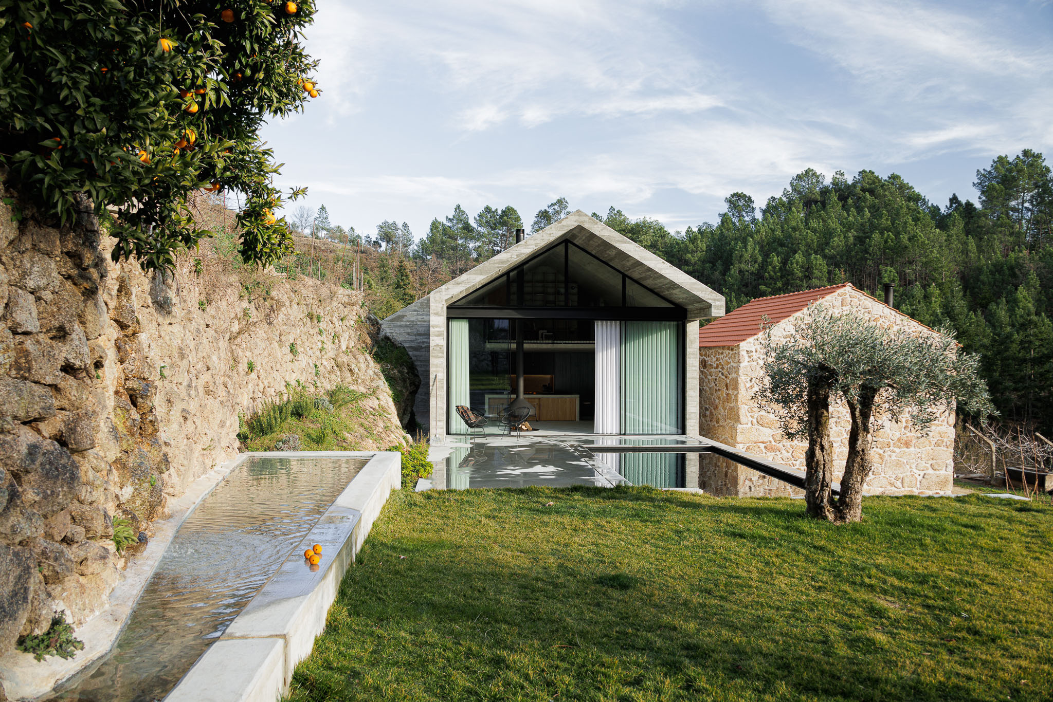 Casa NaMora: Vista exterior da casa com piscina, anexo em pedra e paisagem natural, sob um céu azul. — Casa NaMora arquitetura David Bilo Arquitectos e Filipe Pina Arquitectura em Guarda