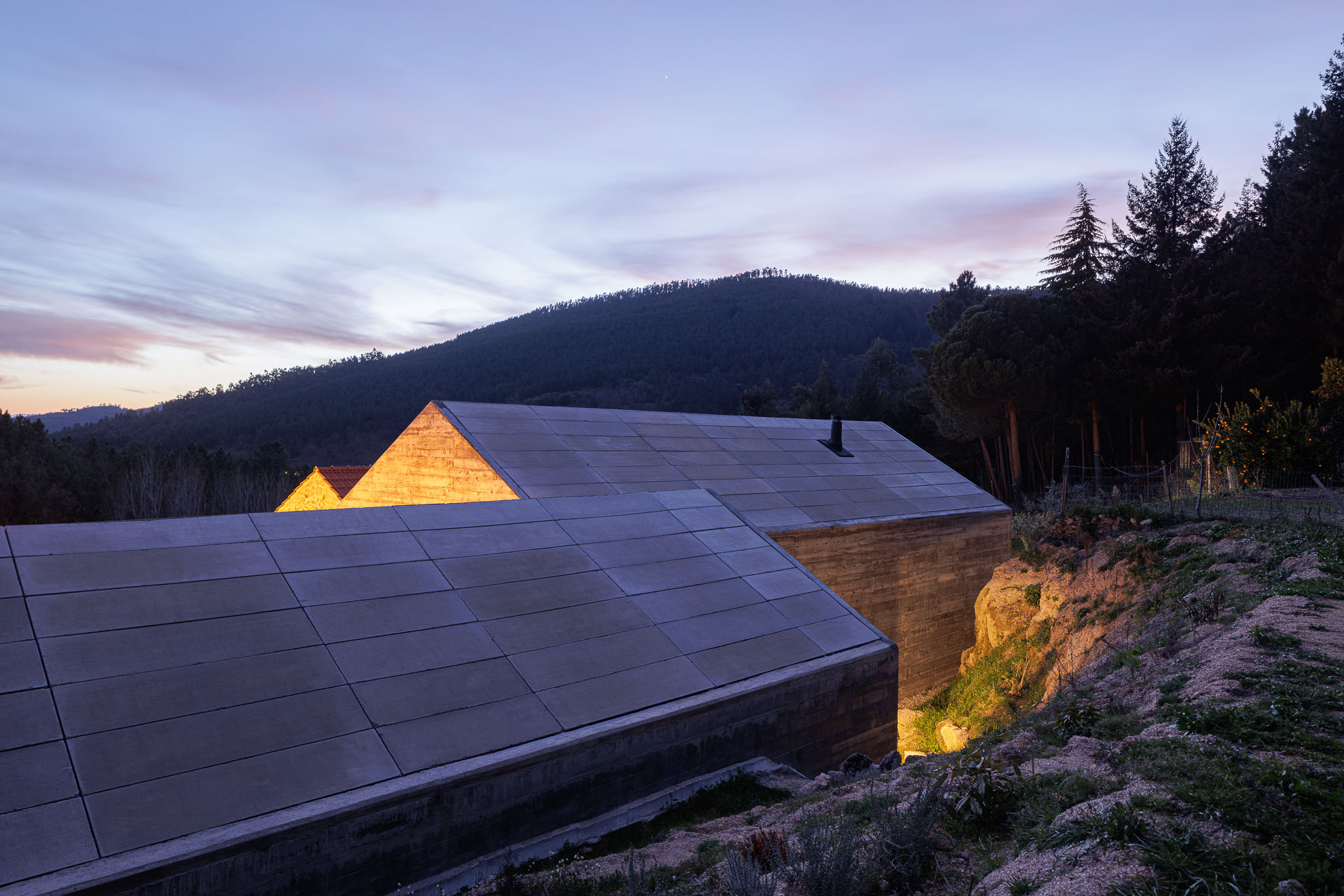 Casa NaMora: Vista noturna da casa com telhado em betão e iluminação indireta, integrada na paisagem montanhosa. — Casa NaMora arquitetura David Bilo Arquitectos e Filipe Pina Arquitectura em Guarda
