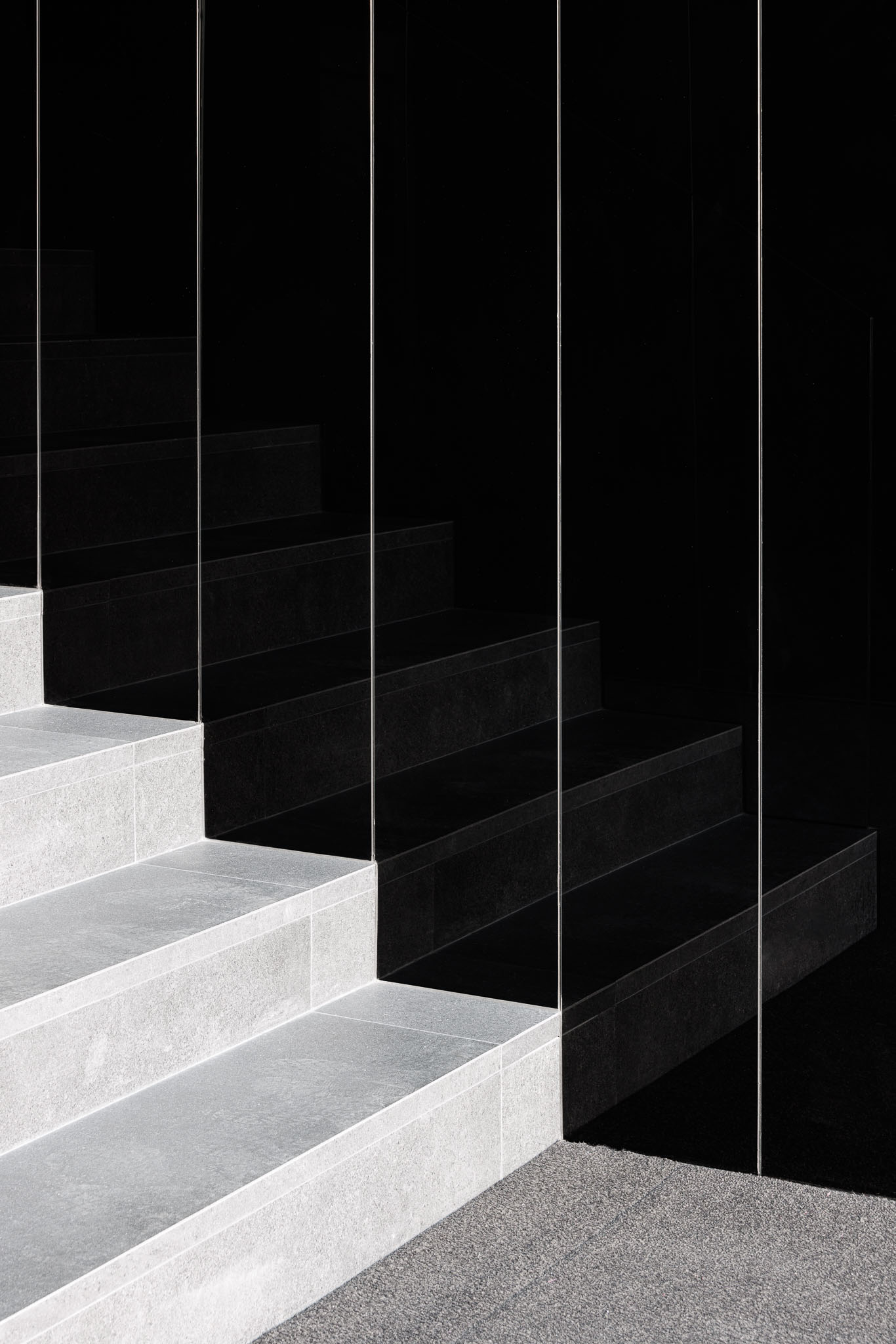 Escada interior com degraus cinzentos e parede preta espelhada, com iluminação minimalista e design moderno. — Puro Homes arquitetura Mário Alves Arquitecto em Aveiro