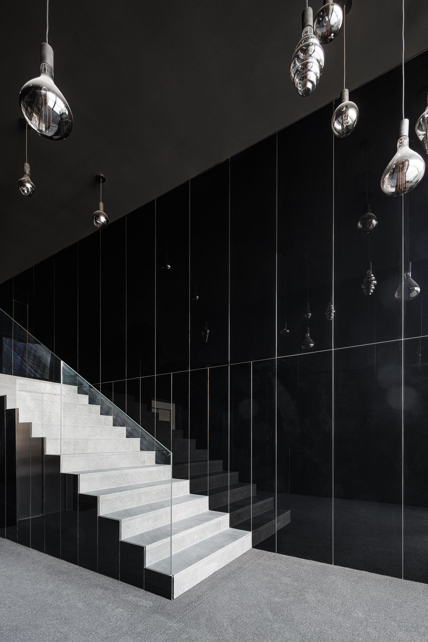 Hall de entrada com escada de pedra cinzenta, parede espelhada preta e candeeiros pendurados com design contemporâneo. — Puro Homes arquitetura Mário Alves Arquitecto em Aveiro