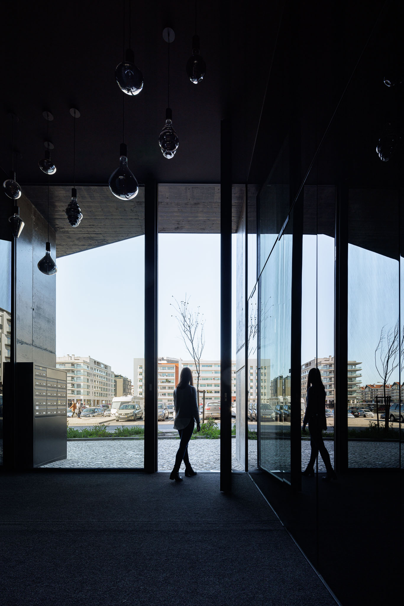 Entrada do edifício com estrutura de vidro e alumínio, silhueta de pessoa e vista para a rua. — Puro Homes arquitetura Mário Alves Arquitecto em Aveiro