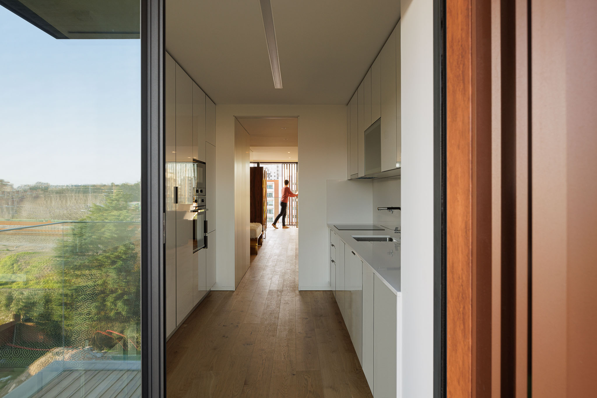 Cozinha moderna com armários brancos, bancada em pedra clara, pavimento em madeira e vista para o exterior. — Puro Homes arquitetura Mário Alves Arquitecto em Aveiro