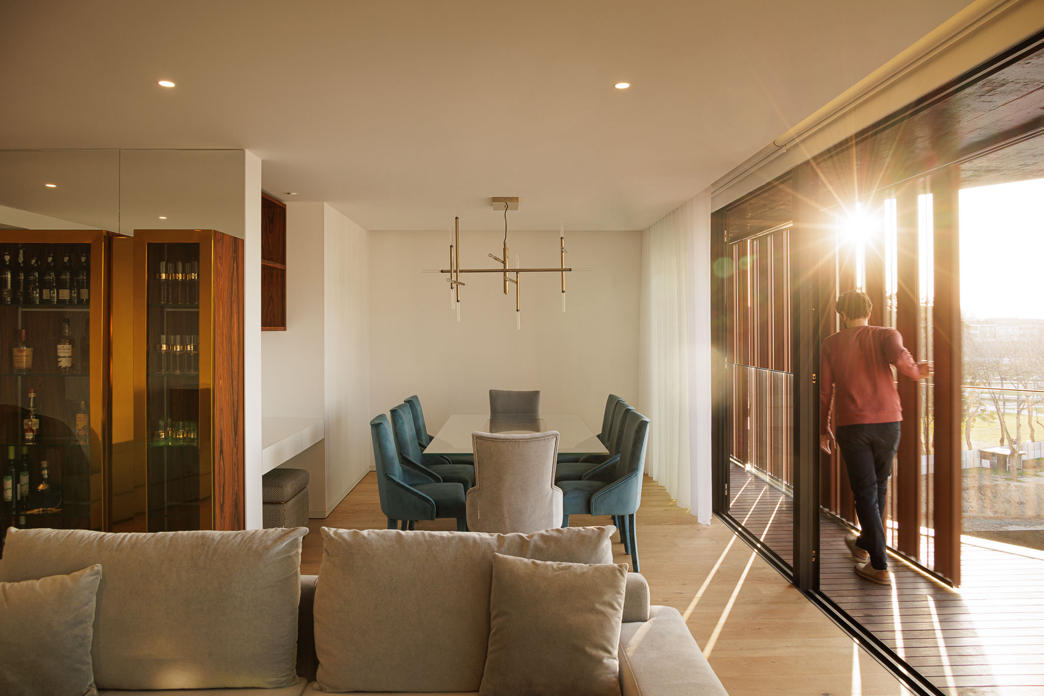 Sala de estar com sofá cinzento, mesa de jantar com cadeiras azuis, armário em madeira e acesso à varanda. — Puro Homes arquitetura Mário Alves Arquitecto em Aveiro