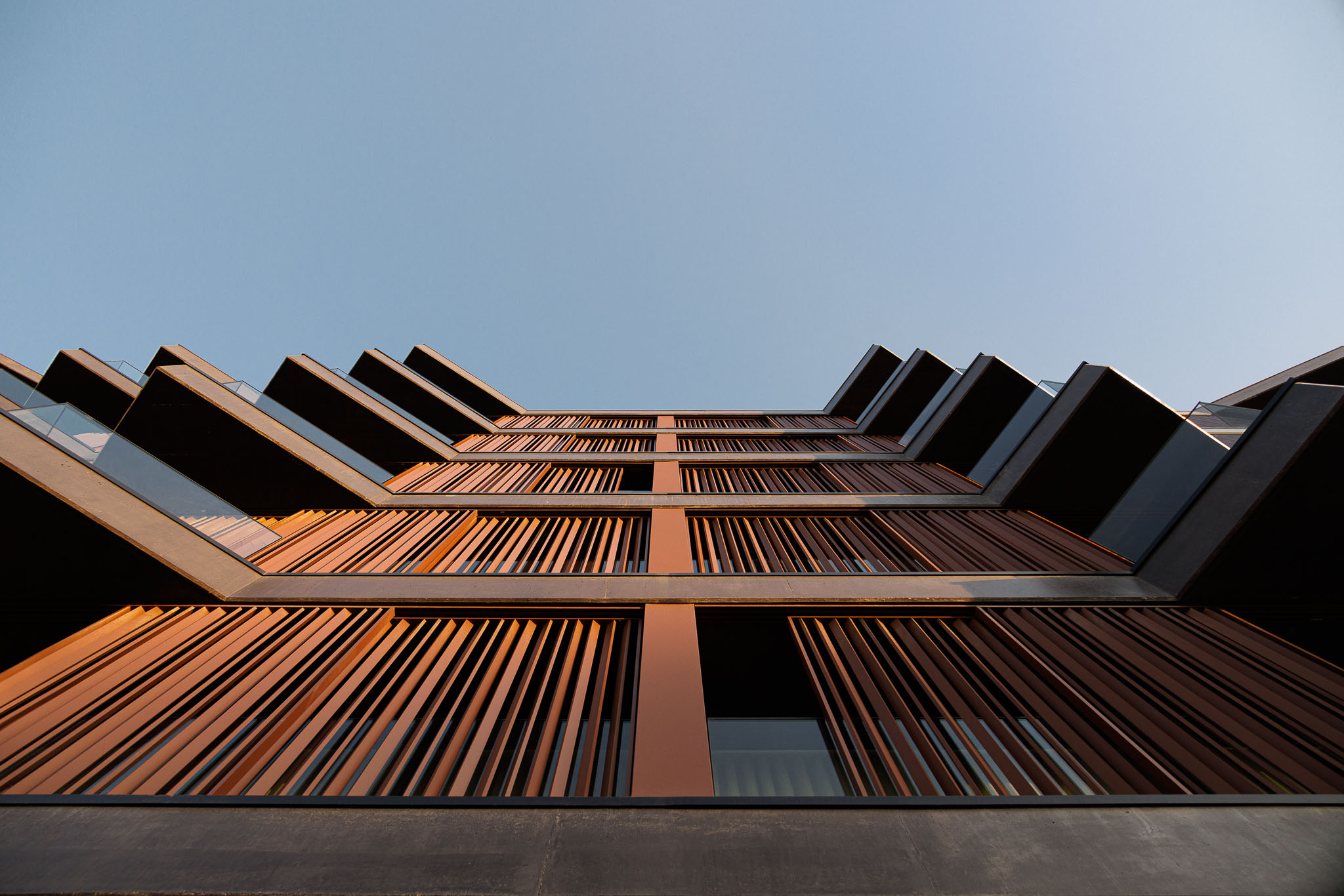 Fachada do edifício com varandas em forma de cunha, revestimento em madeira e céu azul ao fundo. — Puro Homes arquitetura Mário Alves Arquitecto em Aveiro