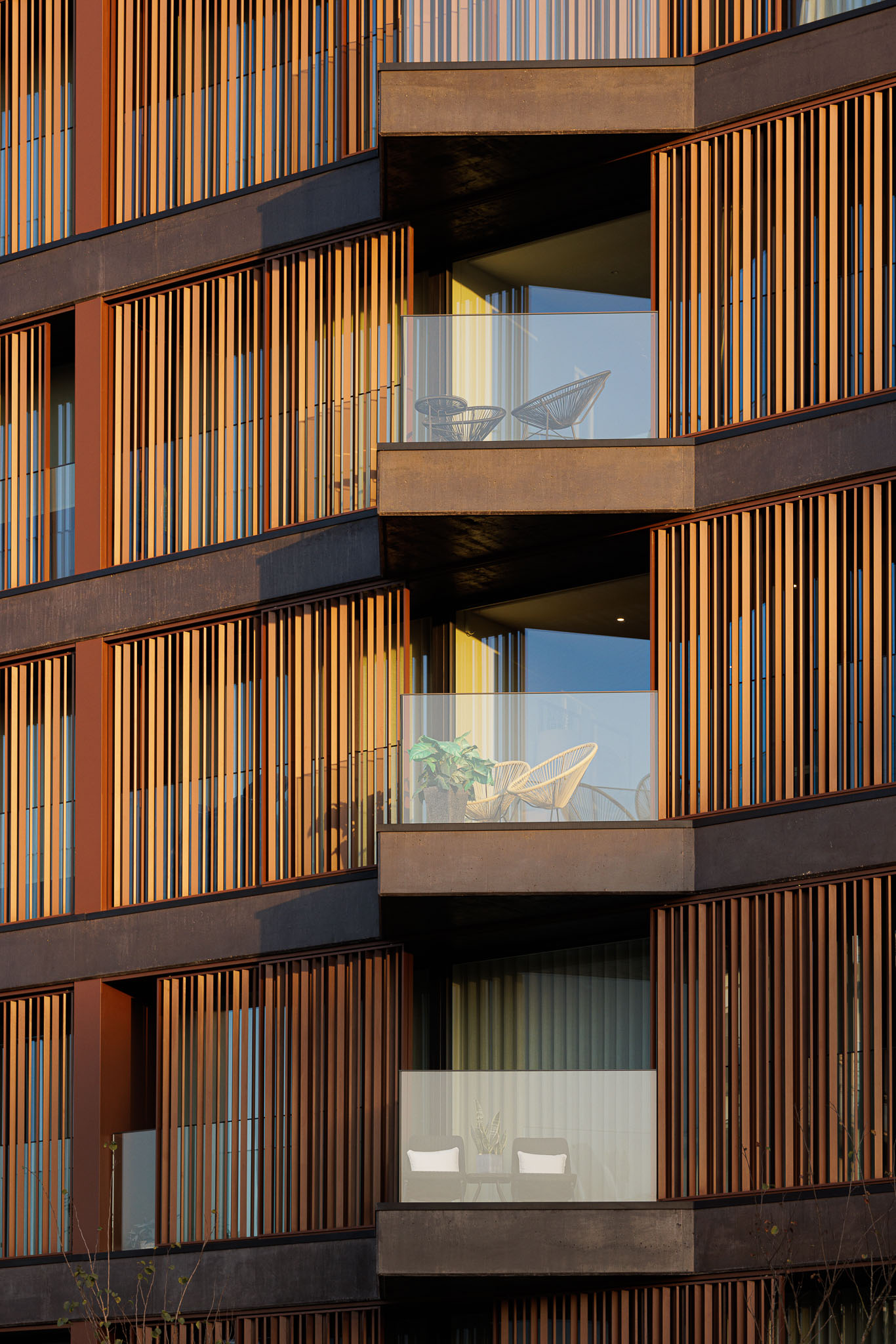 Detalhe da fachada com varandas, ripas de madeira verticais e mobiliário exterior minimalista. — Puro Homes arquitetura Mário Alves Arquitecto em Aveiro