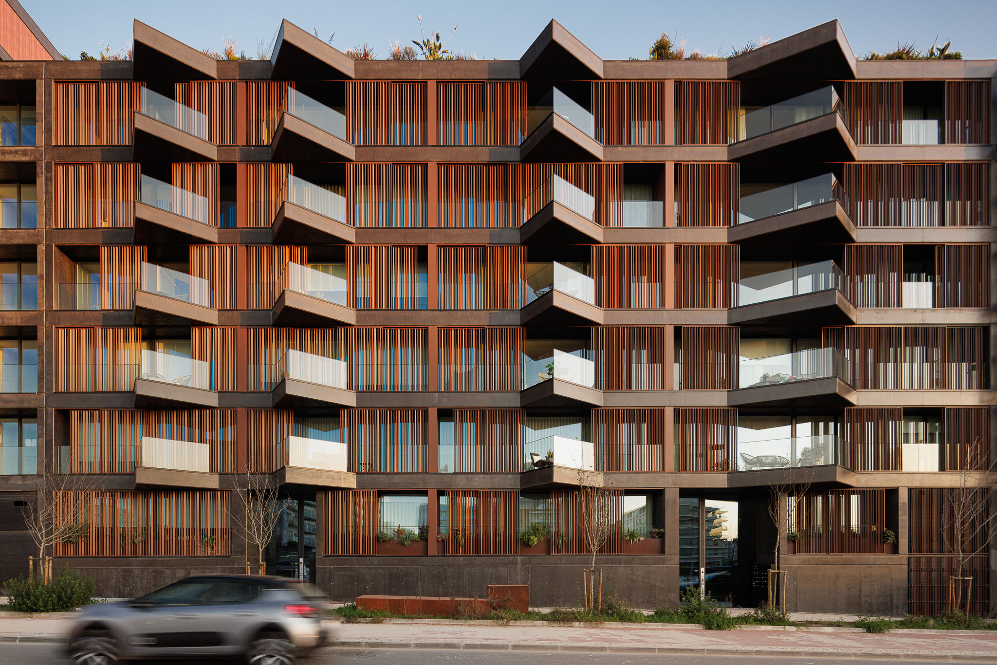 Fachada do edifício com varandas geométricas, revestimento em madeira e vegetação no topo. — Puro Homes arquitetura Mário Alves Arquitecto em Aveiro
