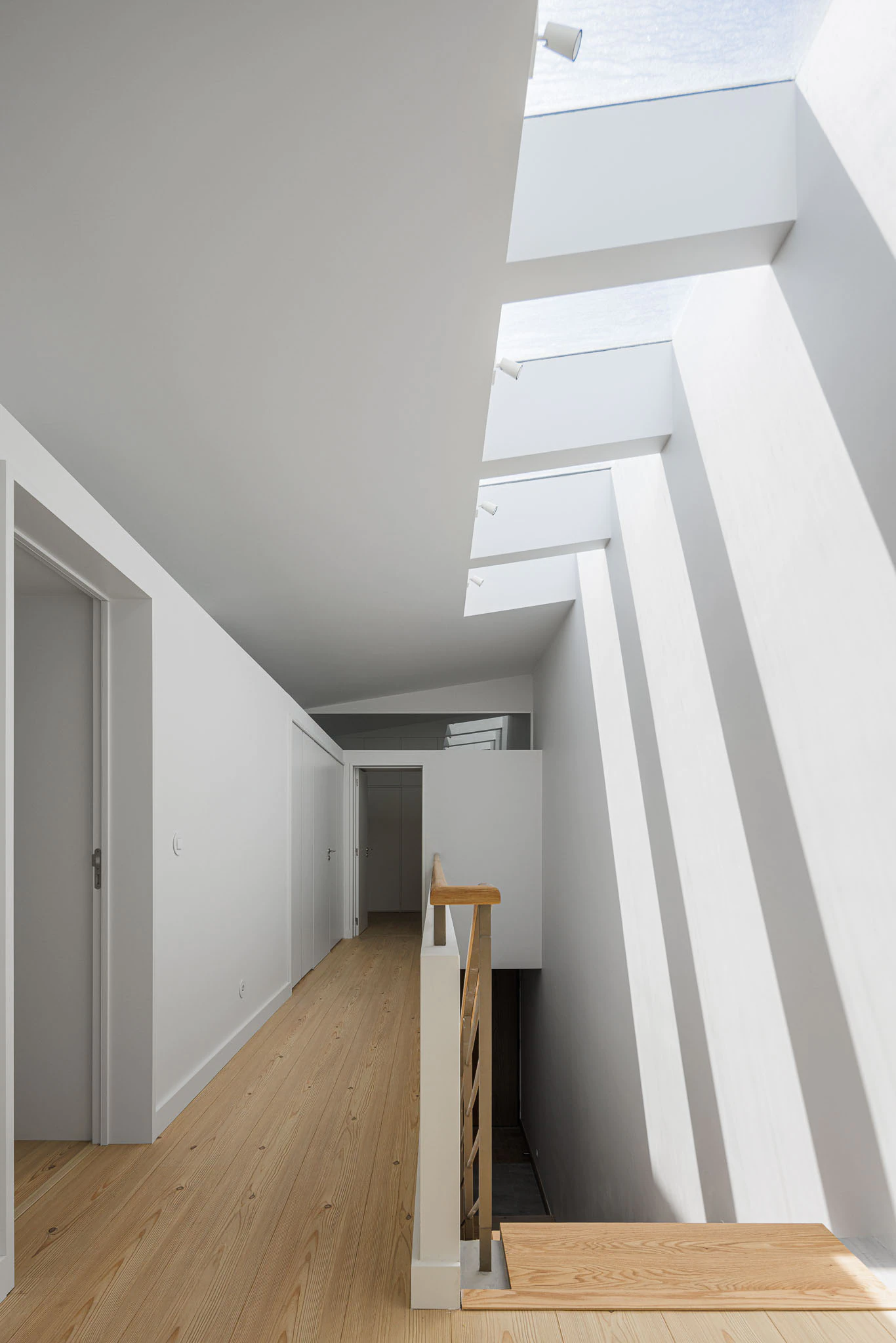 Corredor com claraboias, portas brancas e chão de madeira clara. Design interior que maximiza a iluminação natural. — Casas do Pinhal arquitetura Pk Arquitetos em Estoril