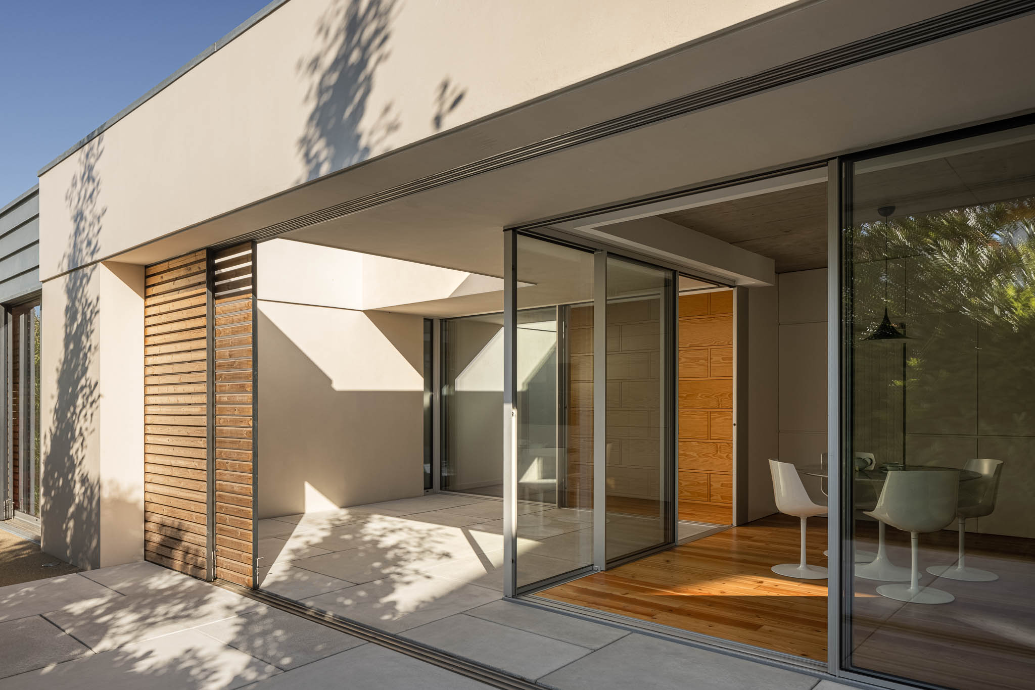 Terraço: Acesso à sala através de grandes janelas deslizantes, com ripas de madeira e pavimento cerâmico. — Casa em Ílhavo arquitetura M2Senos Arquitectos em Ílhavo