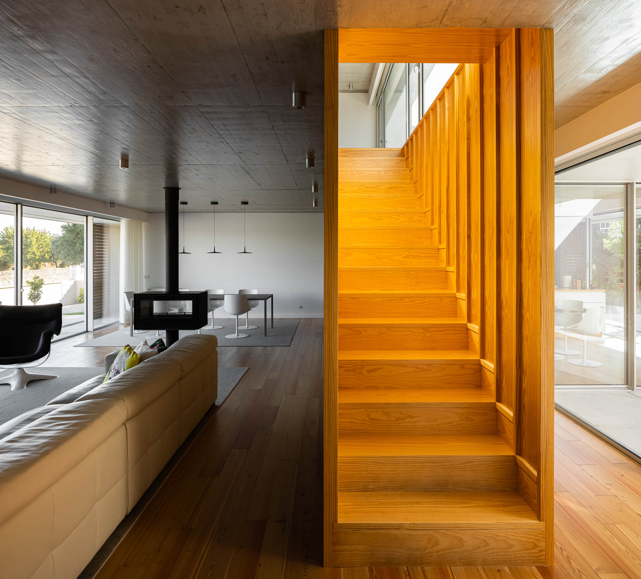 Sala de estar: Escadas em madeira clara, lareira suspensa e vista para a sala de jantar. — Casa em Ílhavo arquitetura M2Senos Arquitectos em Ílhavo