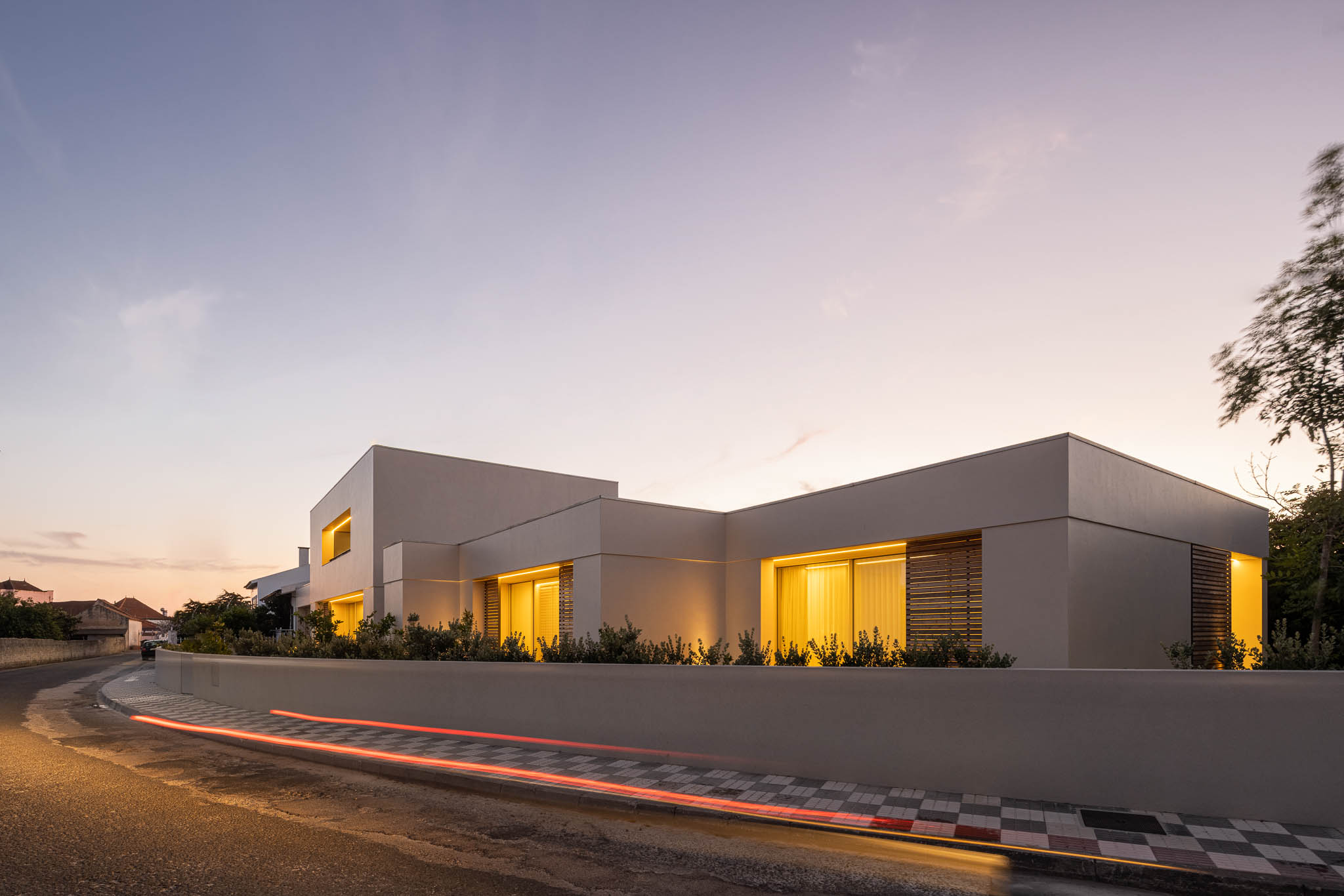 Fachada: Vista noturna da casa com volumes brancos iluminados e jardim frontal. — Casa em Ílhavo arquitetura M2Senos Arquitectos em Ílhavo