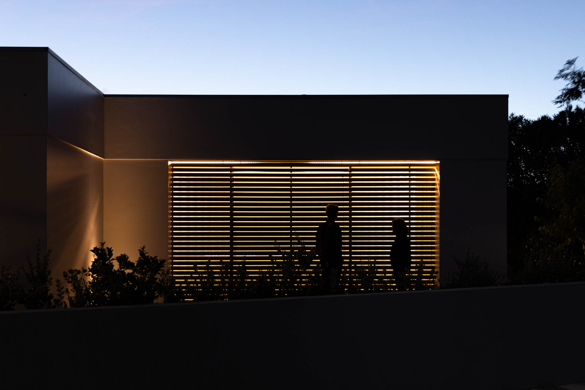 Fachada: Detalhe da janela superior com ripas de madeira e iluminação linear. — Casa em Ílhavo arquitetura M2Senos Arquitectos em Ílhavo