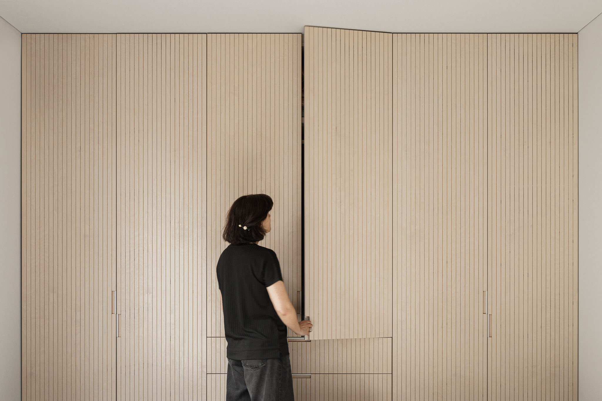 Quarto: Roupeiro em madeira clara canelada, mulher a abrir a porta. — Casa Vertical arquitetura Tsou Arquitectos em Porto