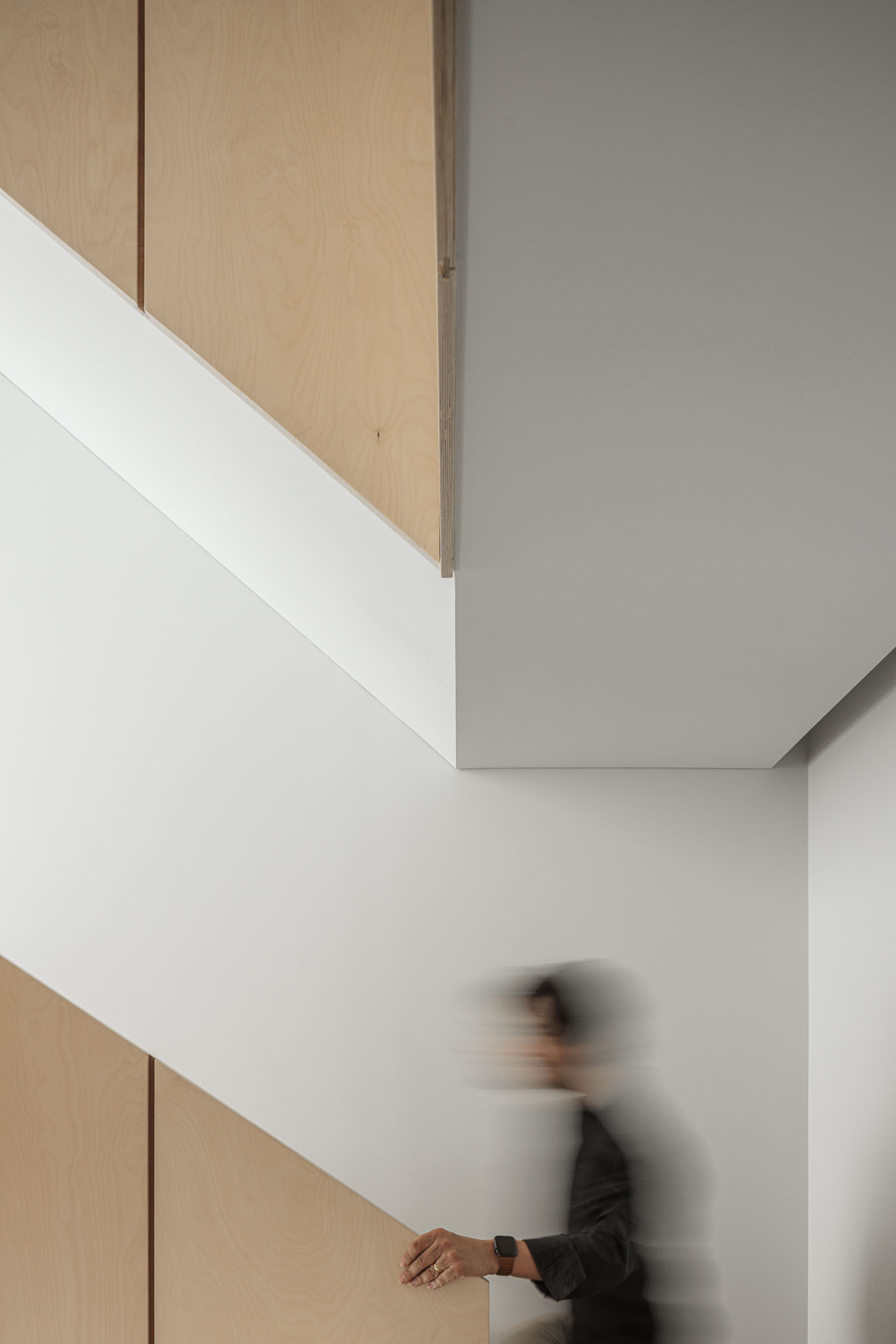 Escada: Corrimão em contraplacado claro, paredes brancas, pessoa a subir as escadas. — Casa Vertical arquitetura Tsou Arquitectos em Porto