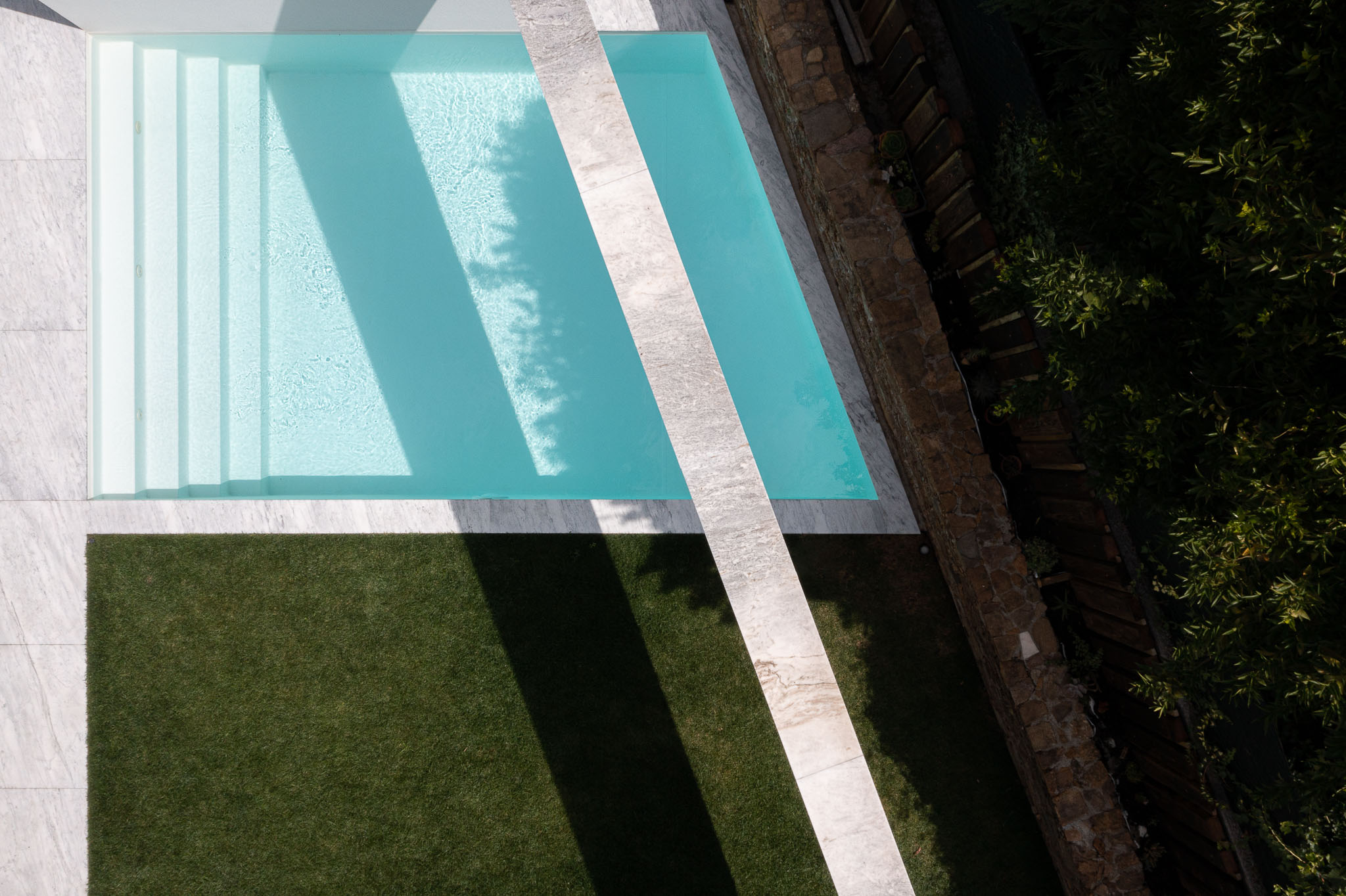 Piscina: Vista aérea da piscina retangular com escadas, relvado e parede em pedra. — Casa Forte arquitetura pema studio em Santo Tirso