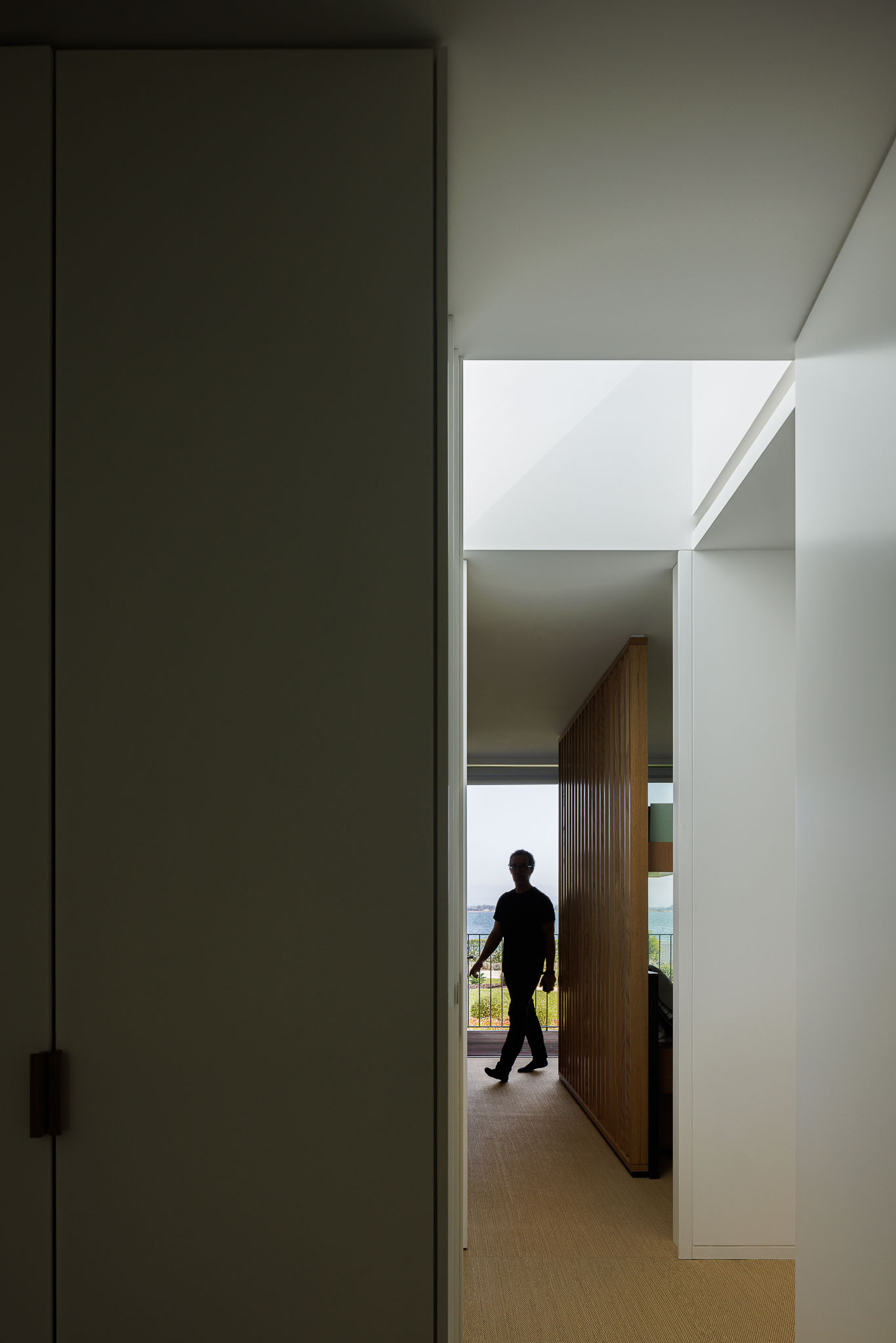 Corredor com paredes brancas, pavimento alcatifado e iluminação zenital. — Casa na Torreira arquitetura Nu.ma em Torreira
