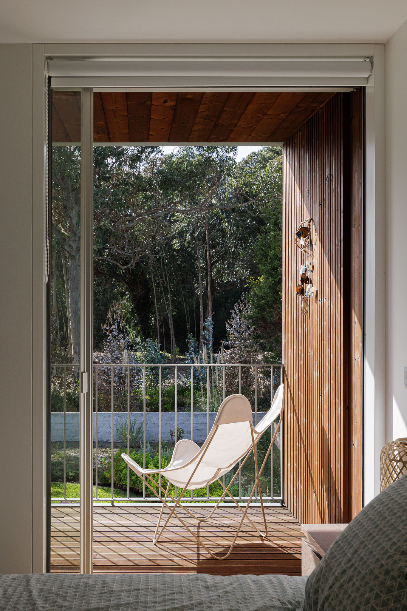 Varanda do quarto com pavimento em madeira, gradeamento metálico e vista para o jardim. — Casa na Torreira arquitetura Nu.ma em Torreira