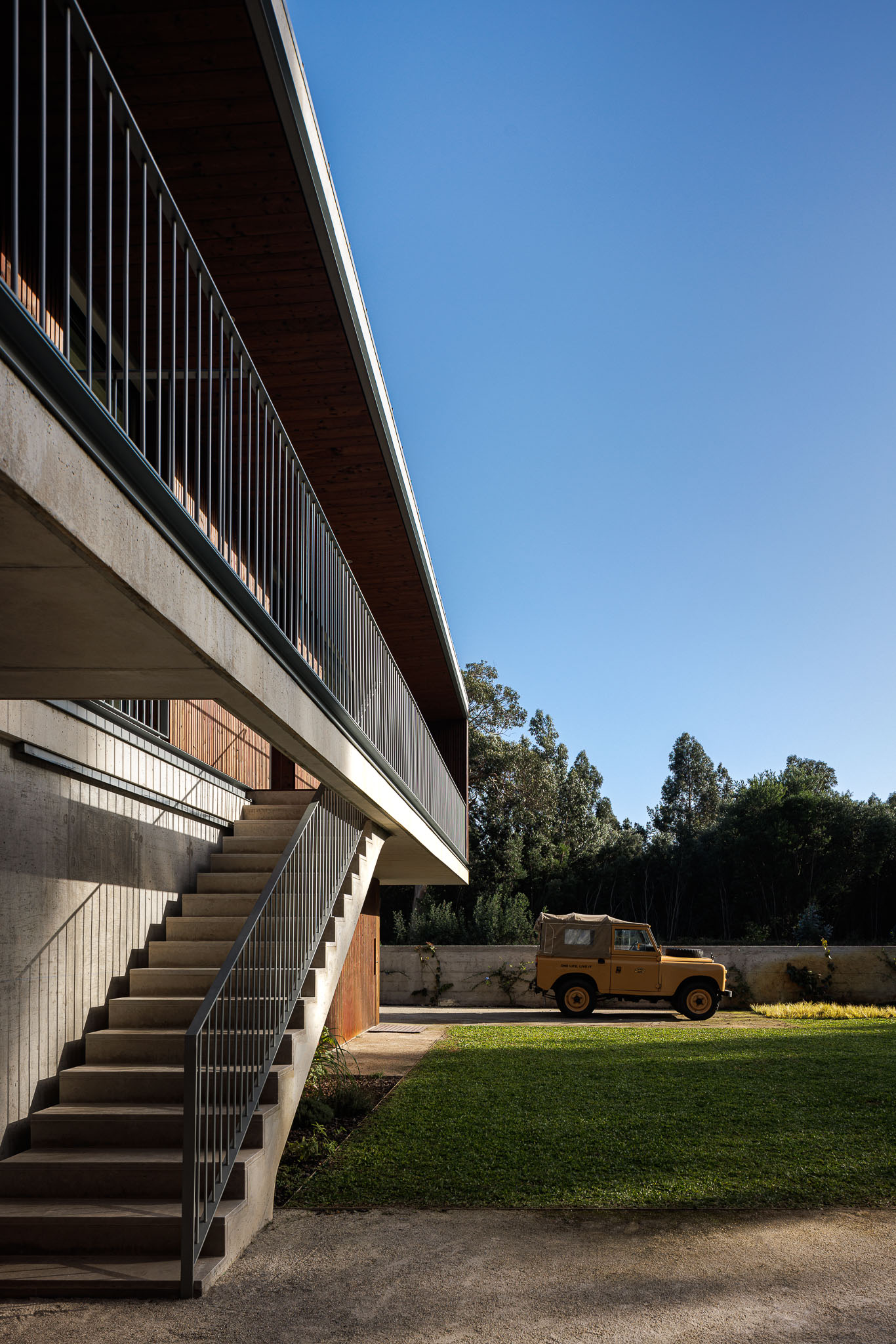 Escadas exteriores em betão, fachada em madeira e carro estacionado no jardim. — Casa na Torreira arquitetura Nu.ma em Torreira