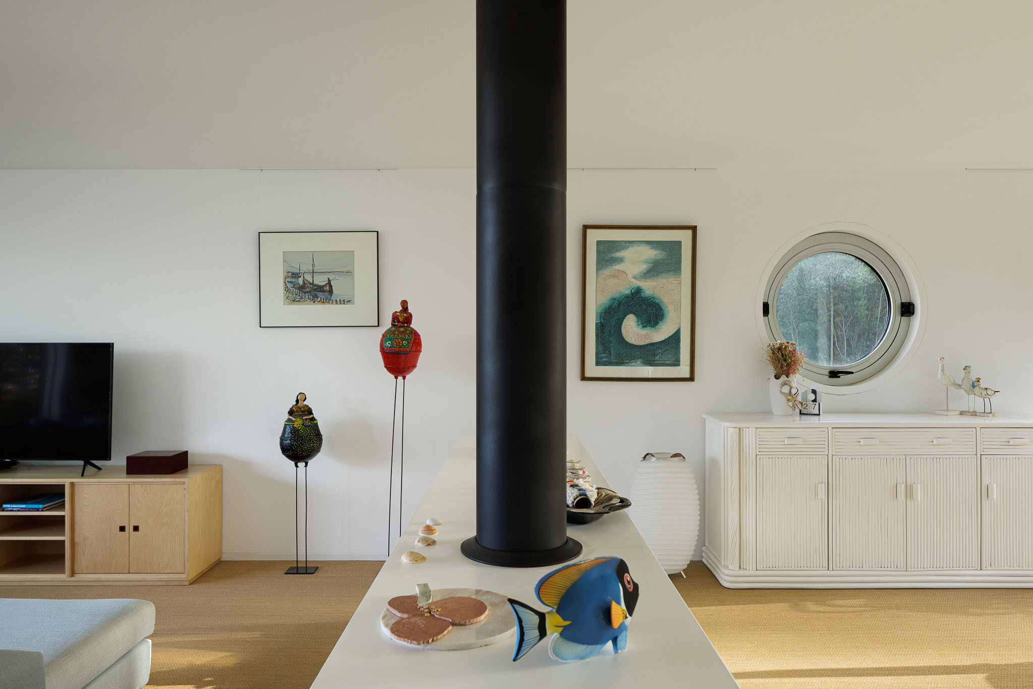 Sala de estar com lareira, móveis de madeira clara e decoração com peças de arte. — Casa na Torreira arquitetura Nu.ma em Torreira