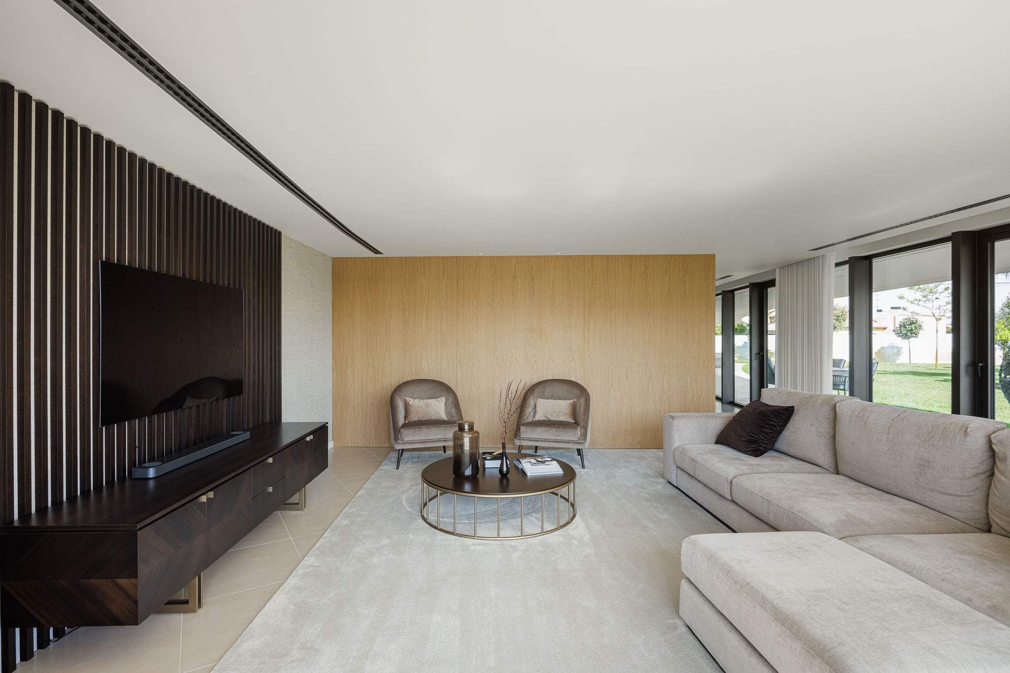 Sala de Estar: Sofá bege, cadeirões de veludo, mesa de centro dourada e painéis de madeira escura na parede. — Casa 109 arquitetura Frari em Vagos