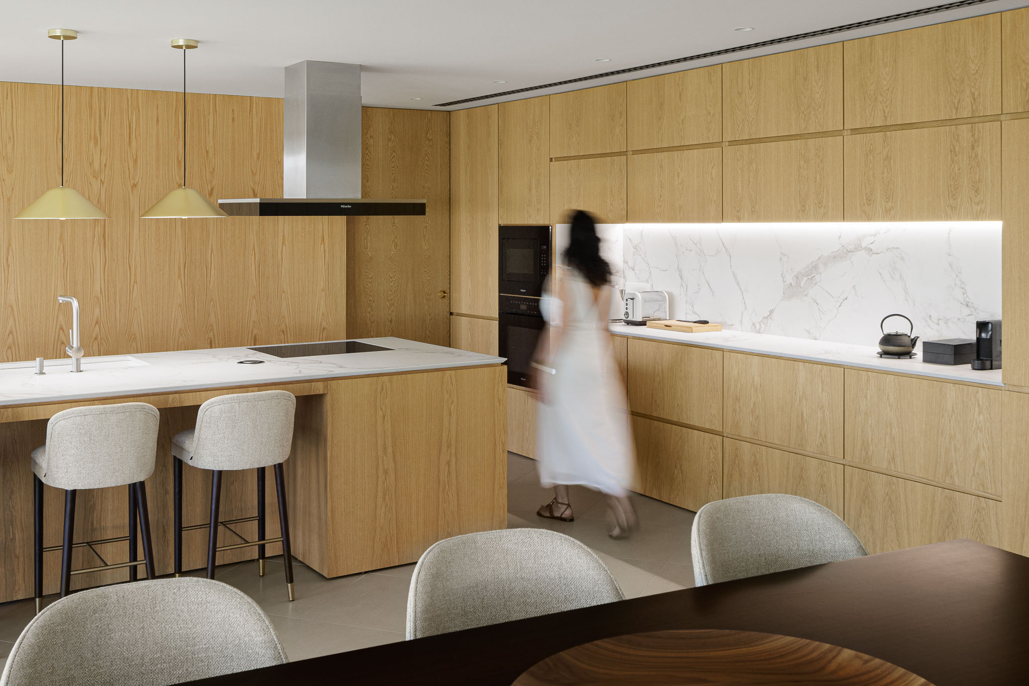 Cozinha: Ilha com bancada branca, armários de madeira clara e candeeiros pendurados. — Casa 109 arquitetura Frari em Vagos