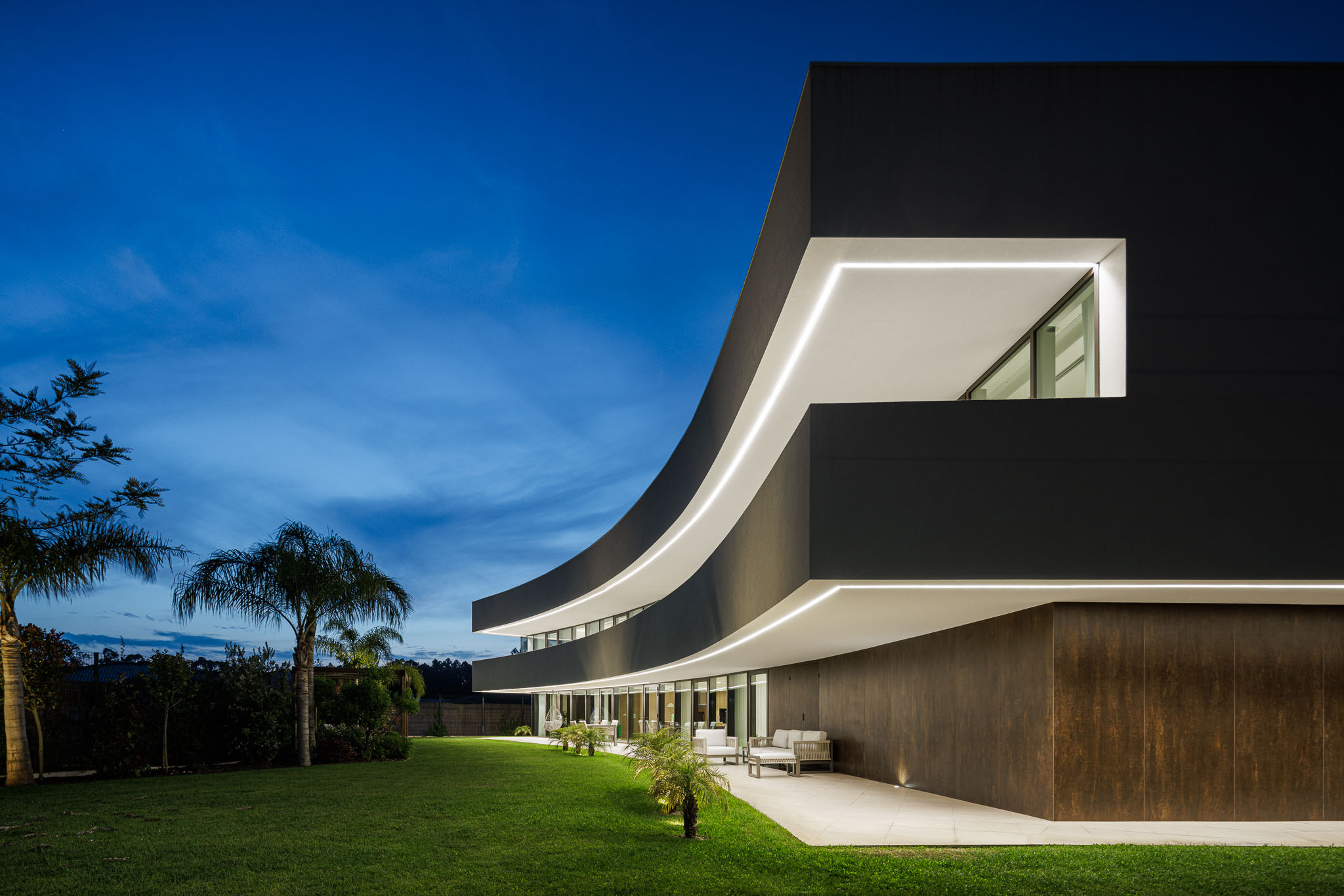 Exterior Noturno: Fachada da casa iluminada à noite, com detalhes curvos e acabamentos em preto e branco. — Casa 109 arquitetura Frari em Vagos