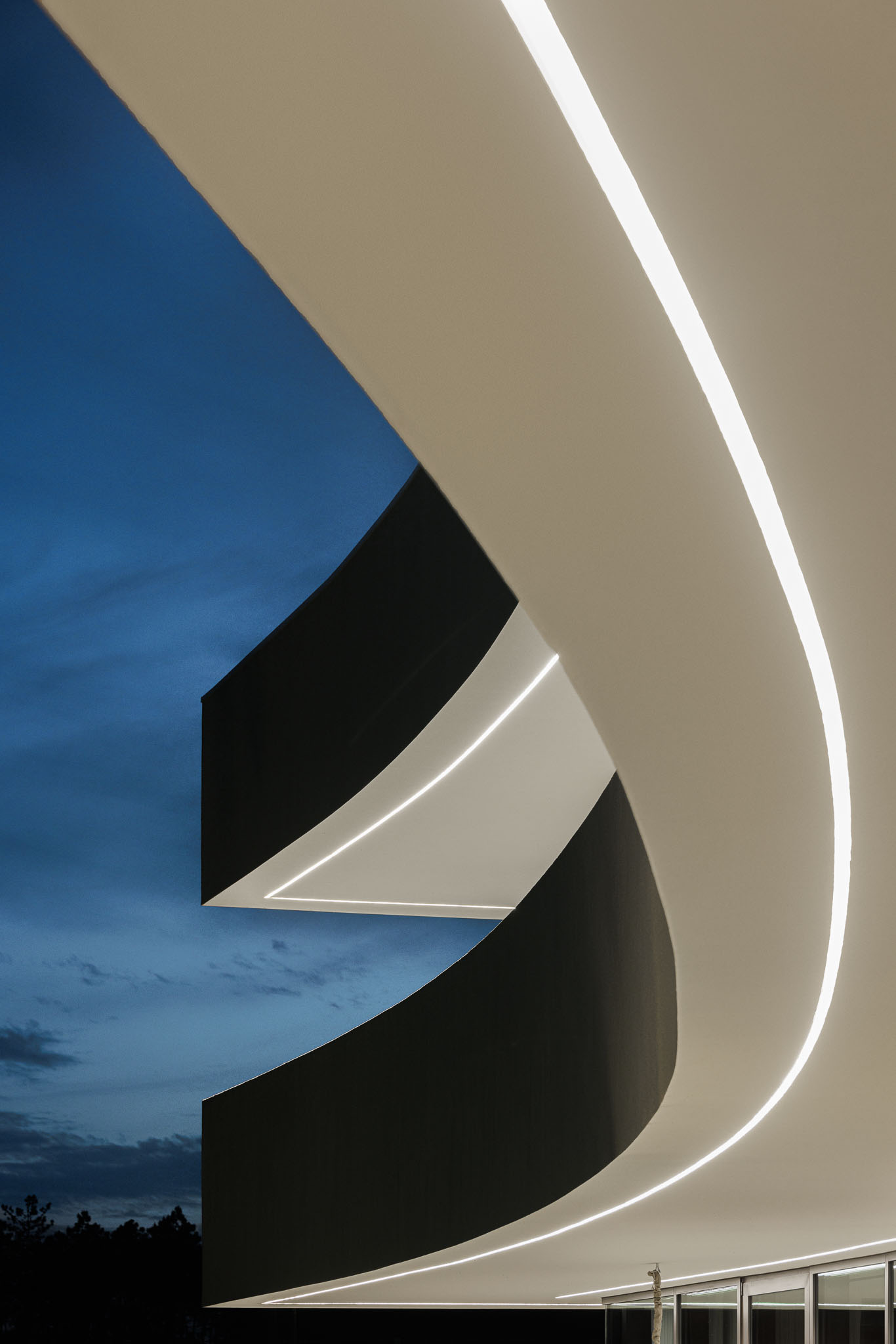 Exterior Noturno: Detalhe da fachada curva iluminada, com acabamentos em preto e branco. — Casa 109 arquitetura Frari em Vagos