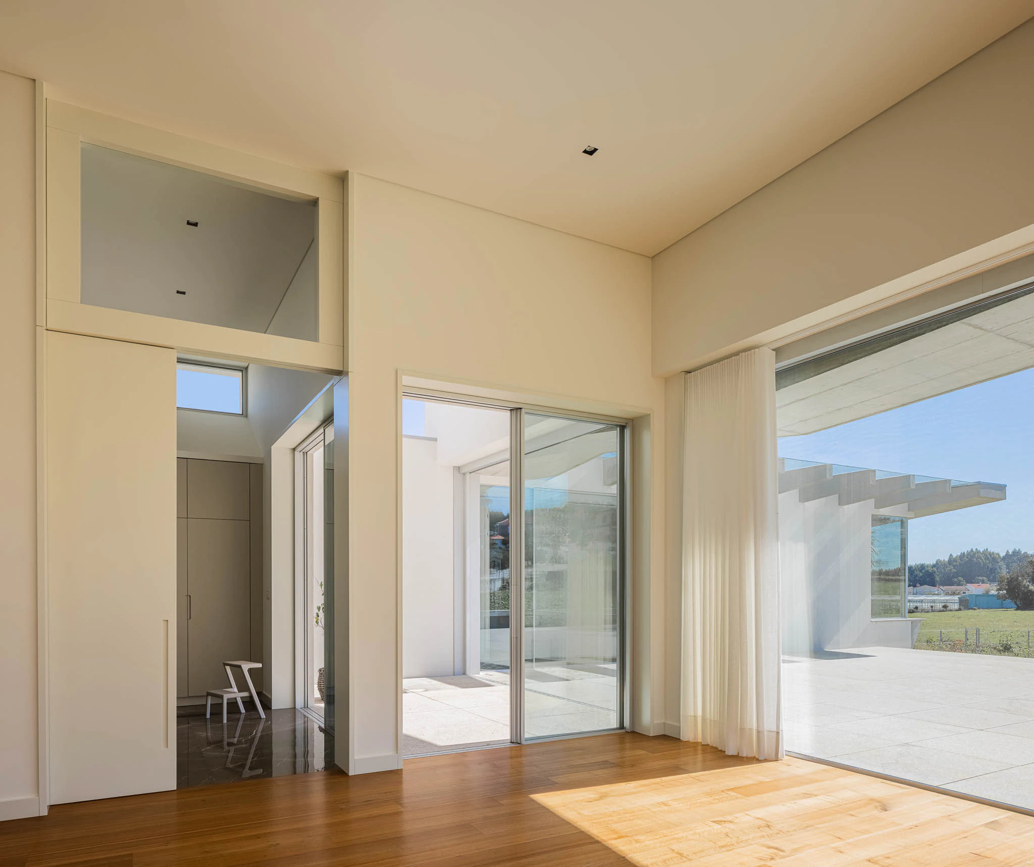Sala luminosa com chão em madeira, grandes janelas para o exterior e design minimalista. — Casa em Brufe arquitetura Oval em Vila Nova de Famalicão