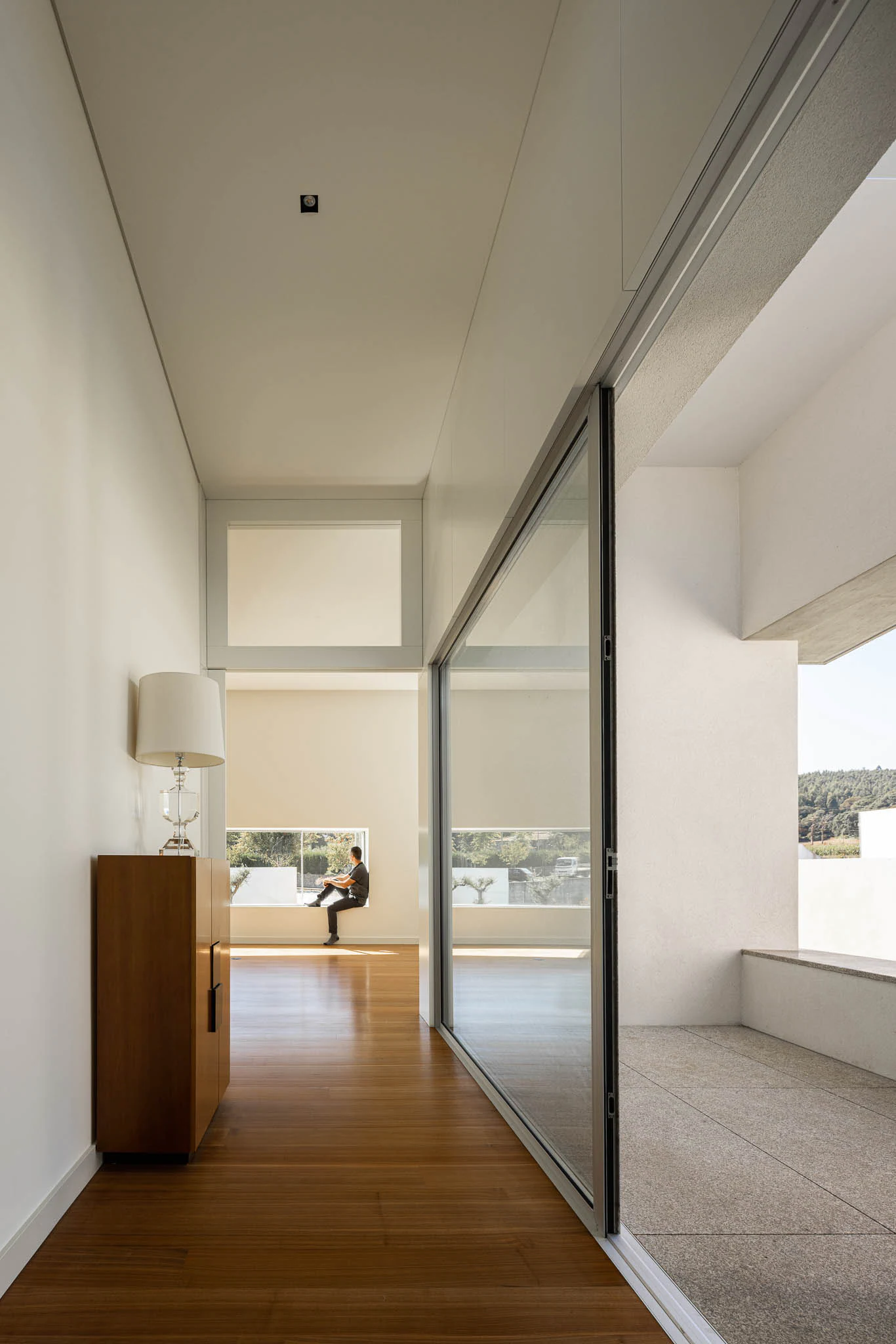Corredor com chão em madeira, porta de correr em vidro e vista para o exterior. — Casa em Brufe arquitetura Oval em Vila Nova de Famalicão