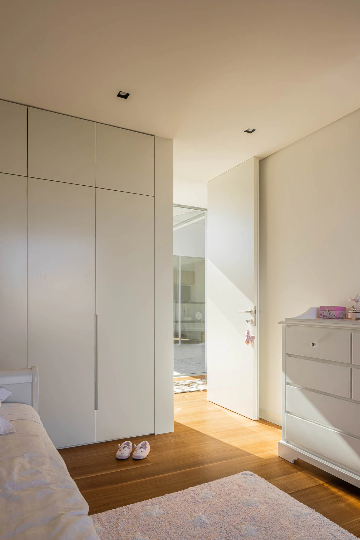 Quarto infantil com roupeiro branco, chão em madeira e detalhes decorativos. — Casa em Brufe arquitetura Oval em Vila Nova de Famalicão