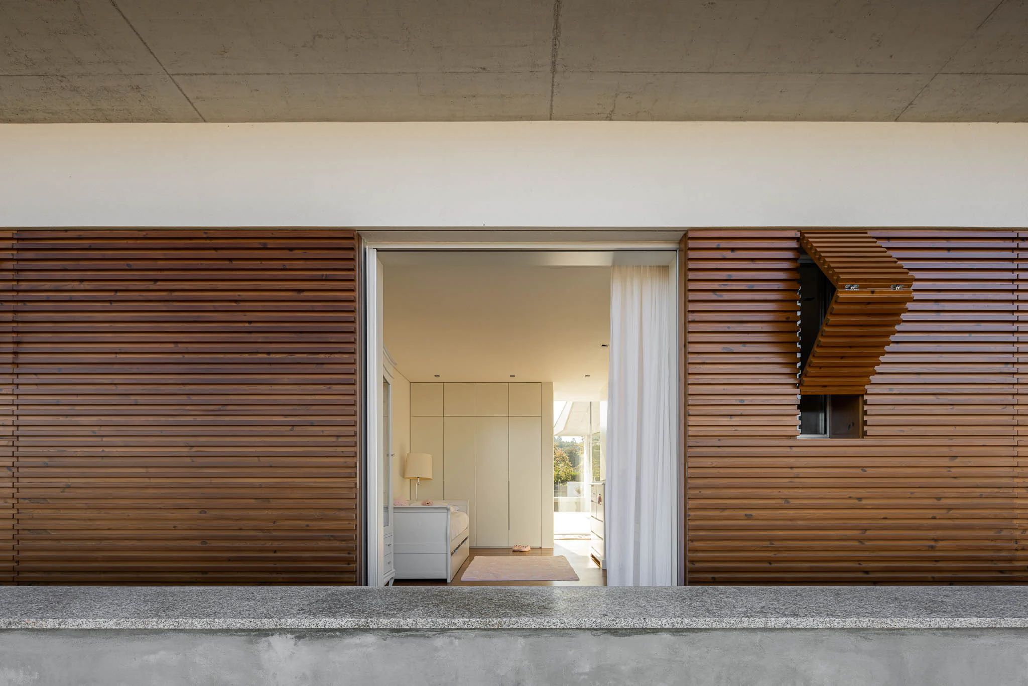 Vista do quarto através de janela com persianas de madeira, design inovador e luz natural. — Casa em Brufe arquitetura Oval em Vila Nova de Famalicão
