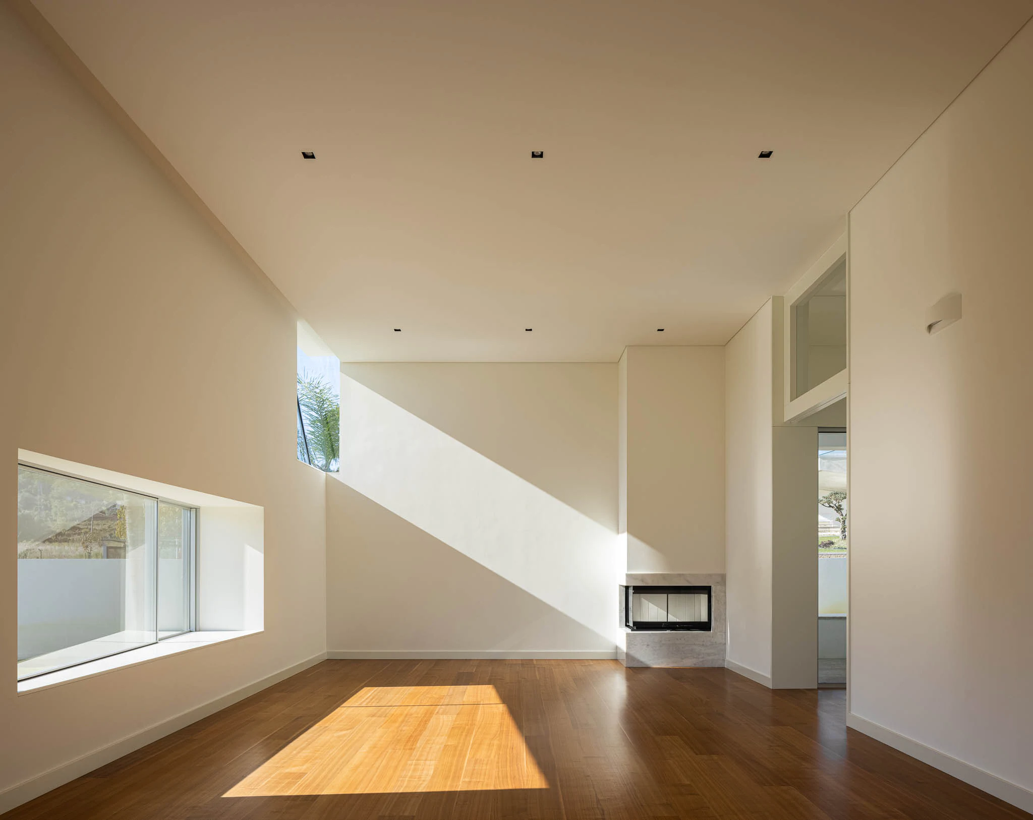 Sala ampla com lareira, janelas geométricas e chão em madeira, com luz natural. — Casa em Brufe arquitetura Oval em Vila Nova de Famalicão