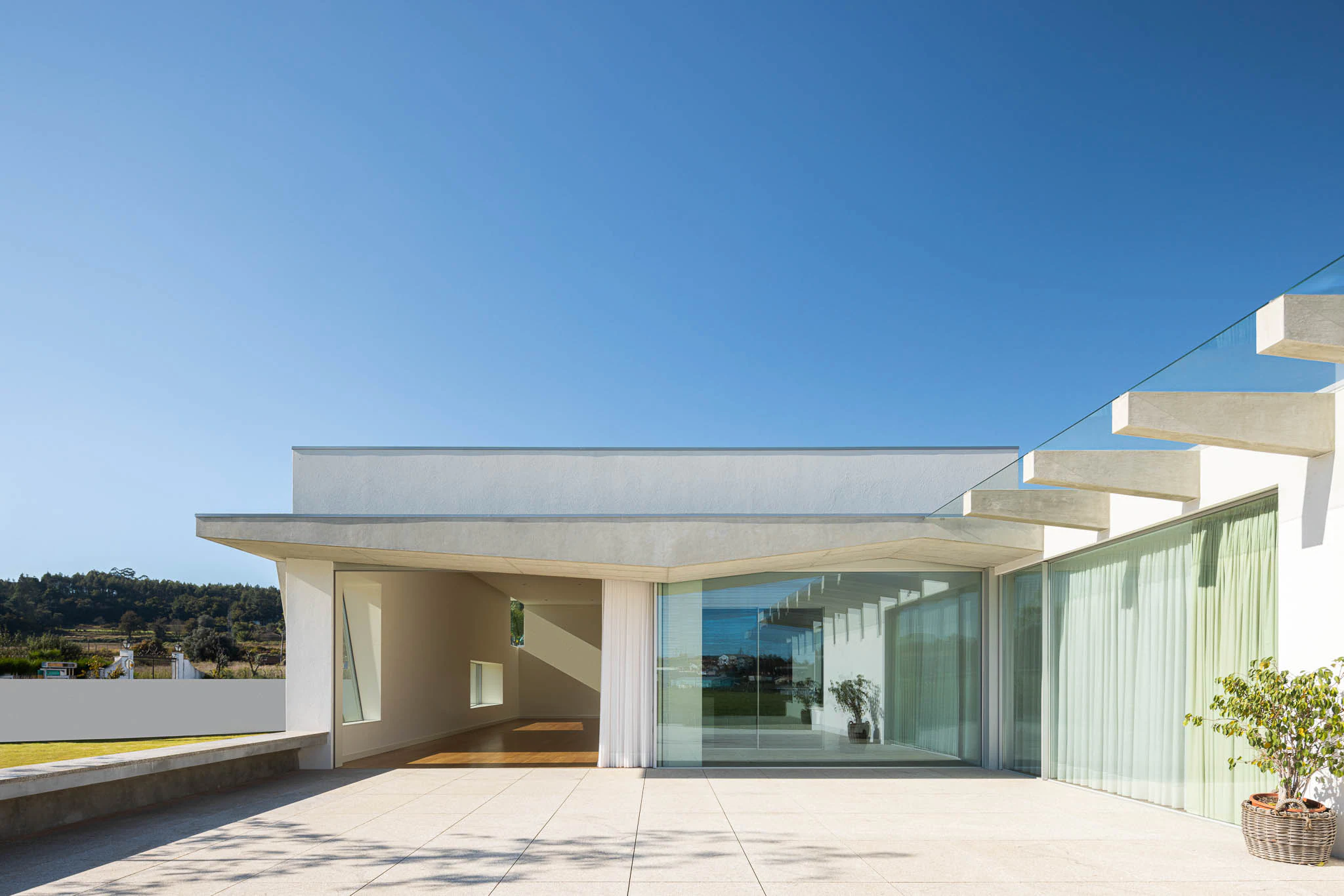 Terraço com vista para o jardim, janelas amplas e design minimalista, com luz natural. — Casa em Brufe arquitetura Oval em Vila Nova de Famalicão