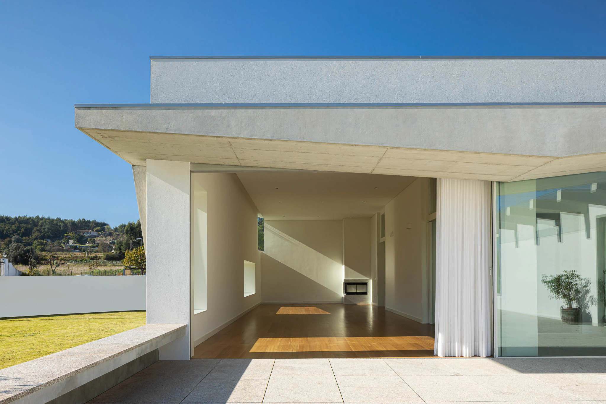 Sala de estar com janelas geométricas, lareira e chão em madeira, com luz natural. — Casa em Brufe arquitetura Oval em Vila Nova de Famalicão