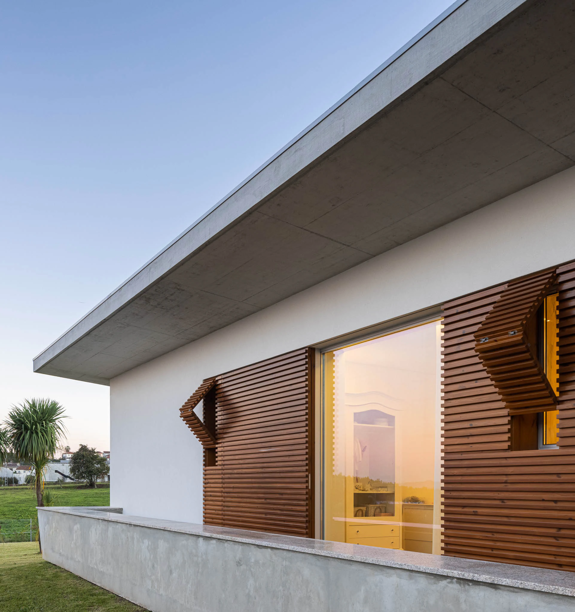 Fachada com janelas amplas e persianas de madeira, iluminação interior e exterior. — Casa em Brufe arquitetura Oval em Vila Nova de Famalicão