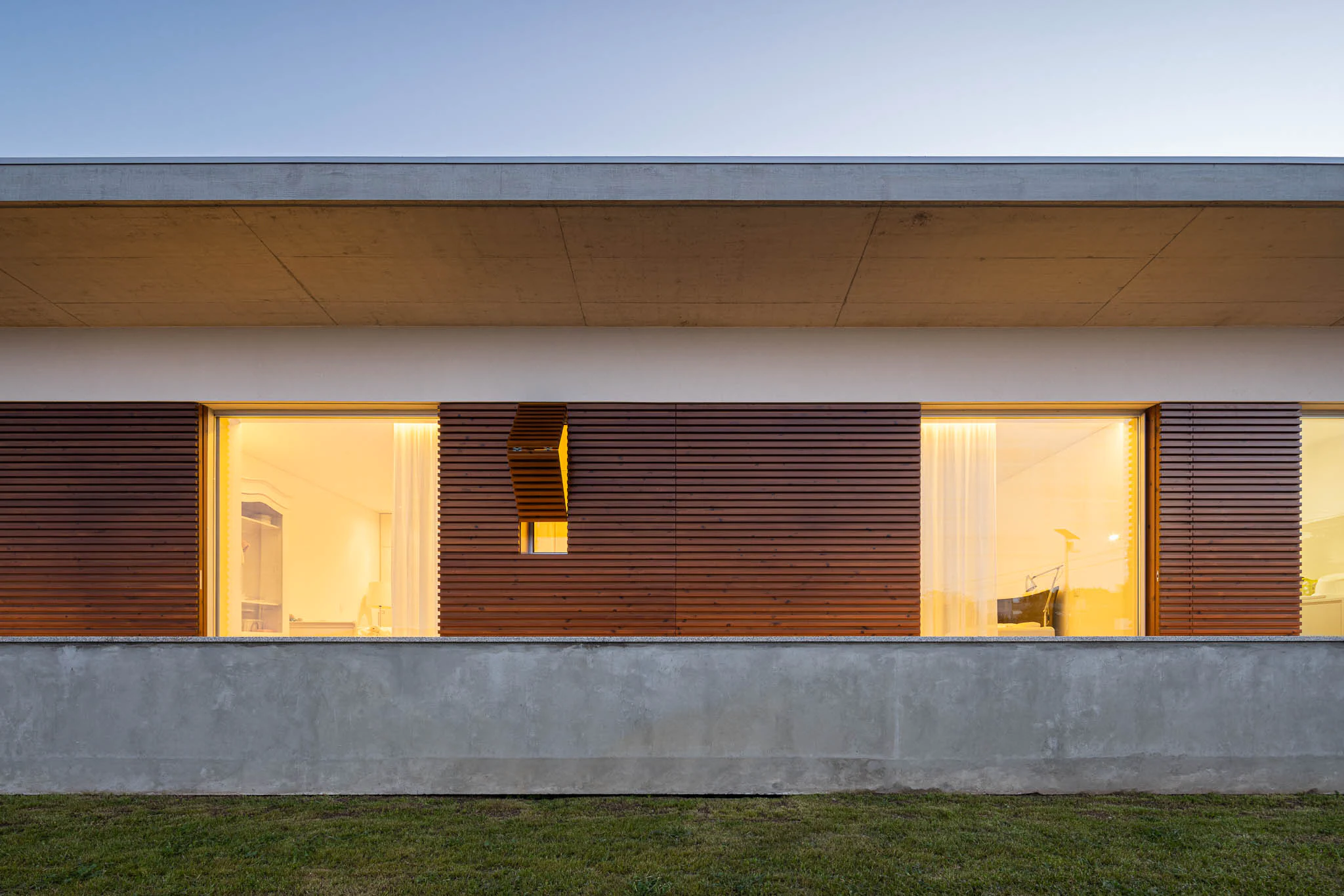 Fachada minimalista com janelas geométricas e iluminação noturna, sob céu azul escuro. — Casa em Brufe arquitetura Oval em Vila Nova de Famalicão