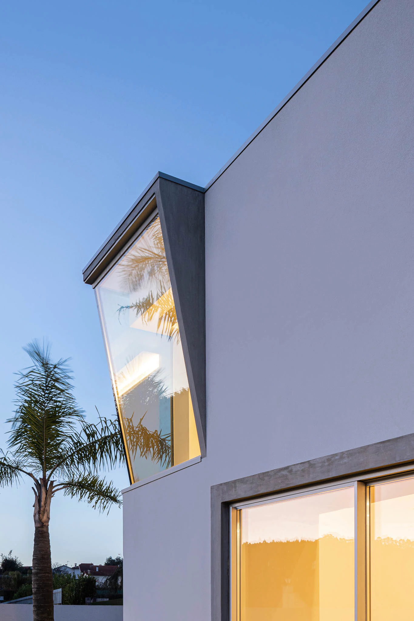 Pormenor da fachada com janelas geométricas, cobertura de betão e iluminação noturna. — Casa em Brufe arquitetura Oval em Vila Nova de Famalicão