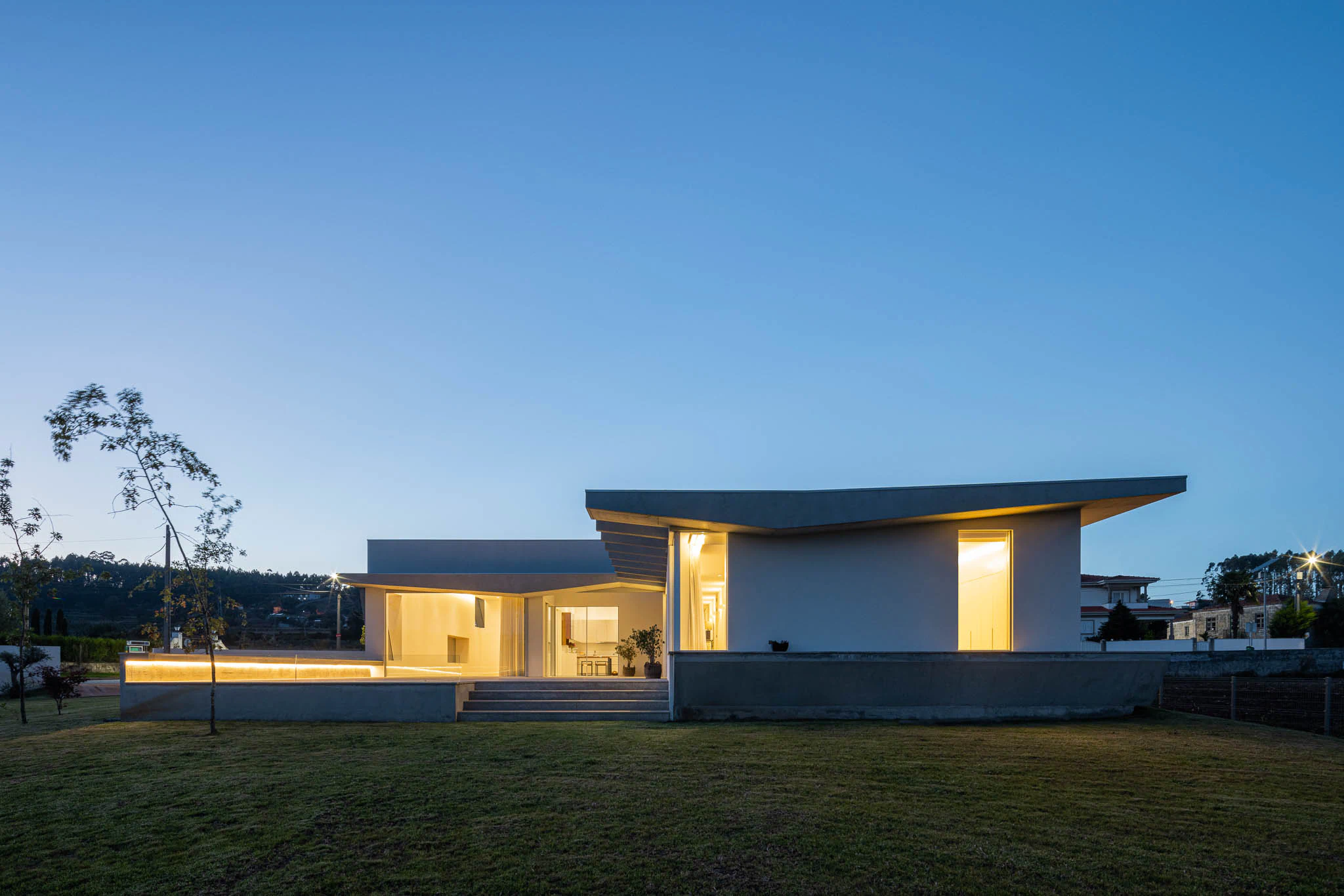 Terraço com iluminação embutida, janelas amplas e vista para o interior da casa. — Casa em Brufe arquitetura Oval em Vila Nova de Famalicão
