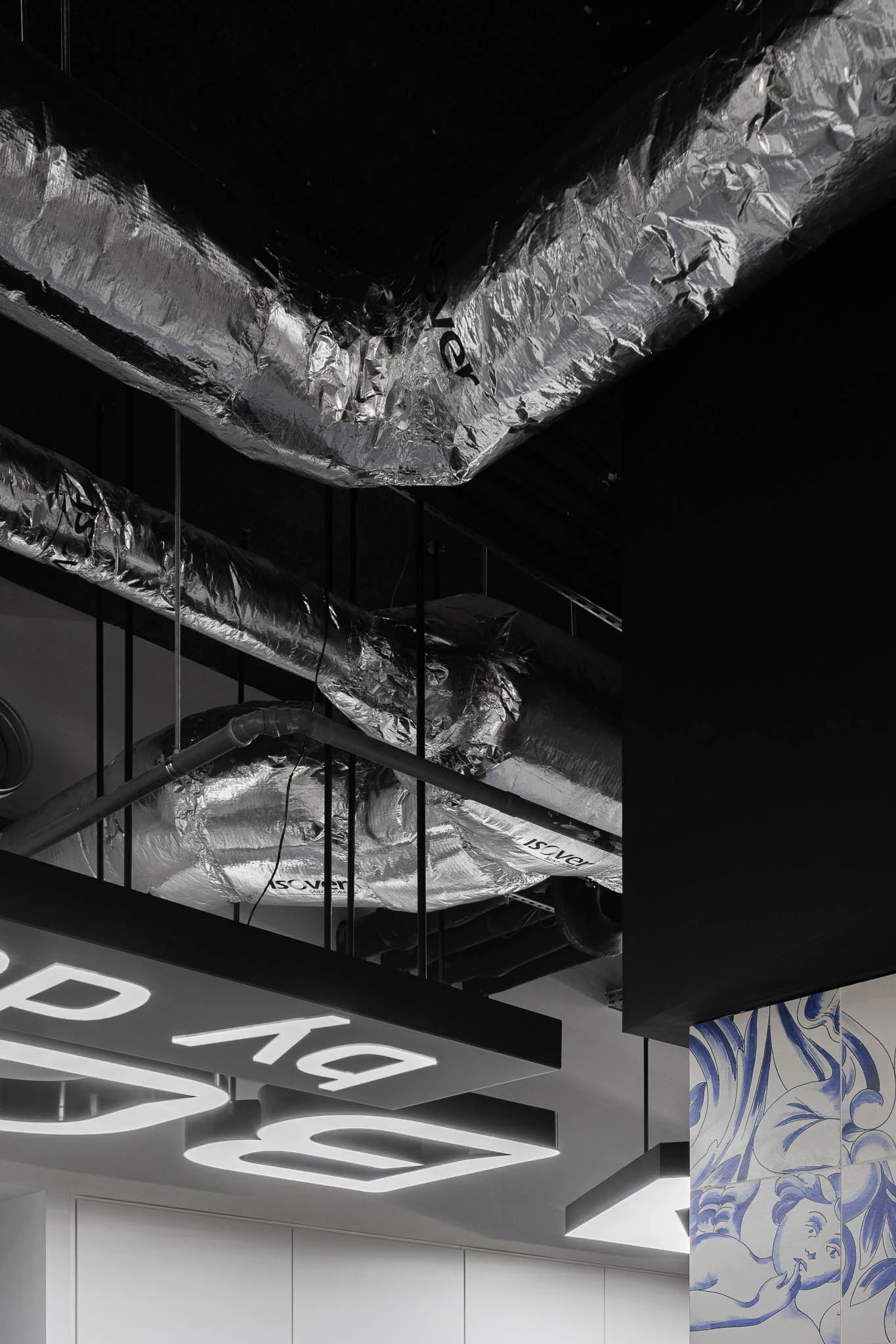 Detalhe de tubagens expostas, iluminação suspensa e padrão de azulejos azuis numa parede branca. — Bold by Devoteam: Escritório Porto arquitetura Inception Architects Studio em Porto