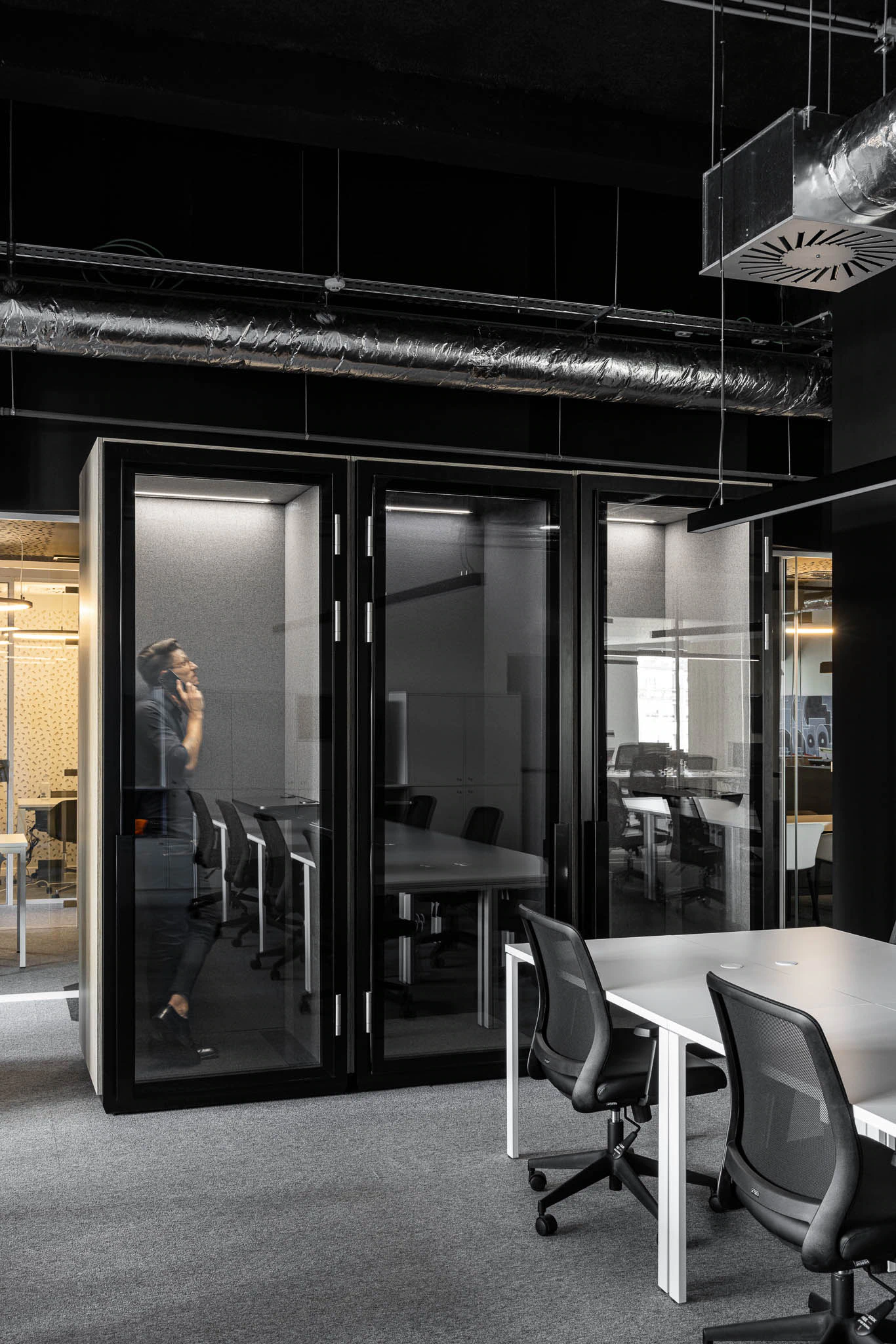 Cabines telefónicas envidraçadas num espaço de trabalho aberto com secretárias brancas e cadeiras pretas. — Bold by Devoteam: Escritório Porto arquitetura Inception Architects Studio em Porto