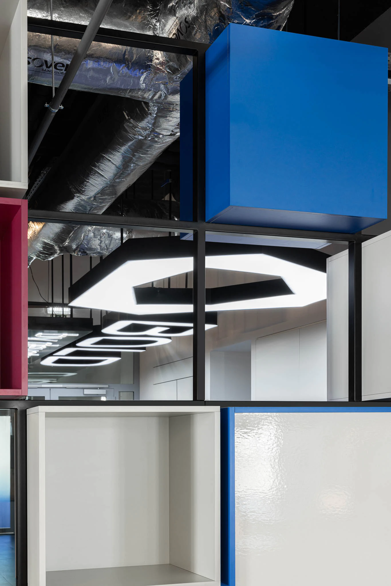 Detalhe de estantes coloridas suspensas, iluminação hexagonal e tubagens industriais expostas. — Bold by Devoteam: Escritório Porto arquitetura Inception Architects Studio em Porto