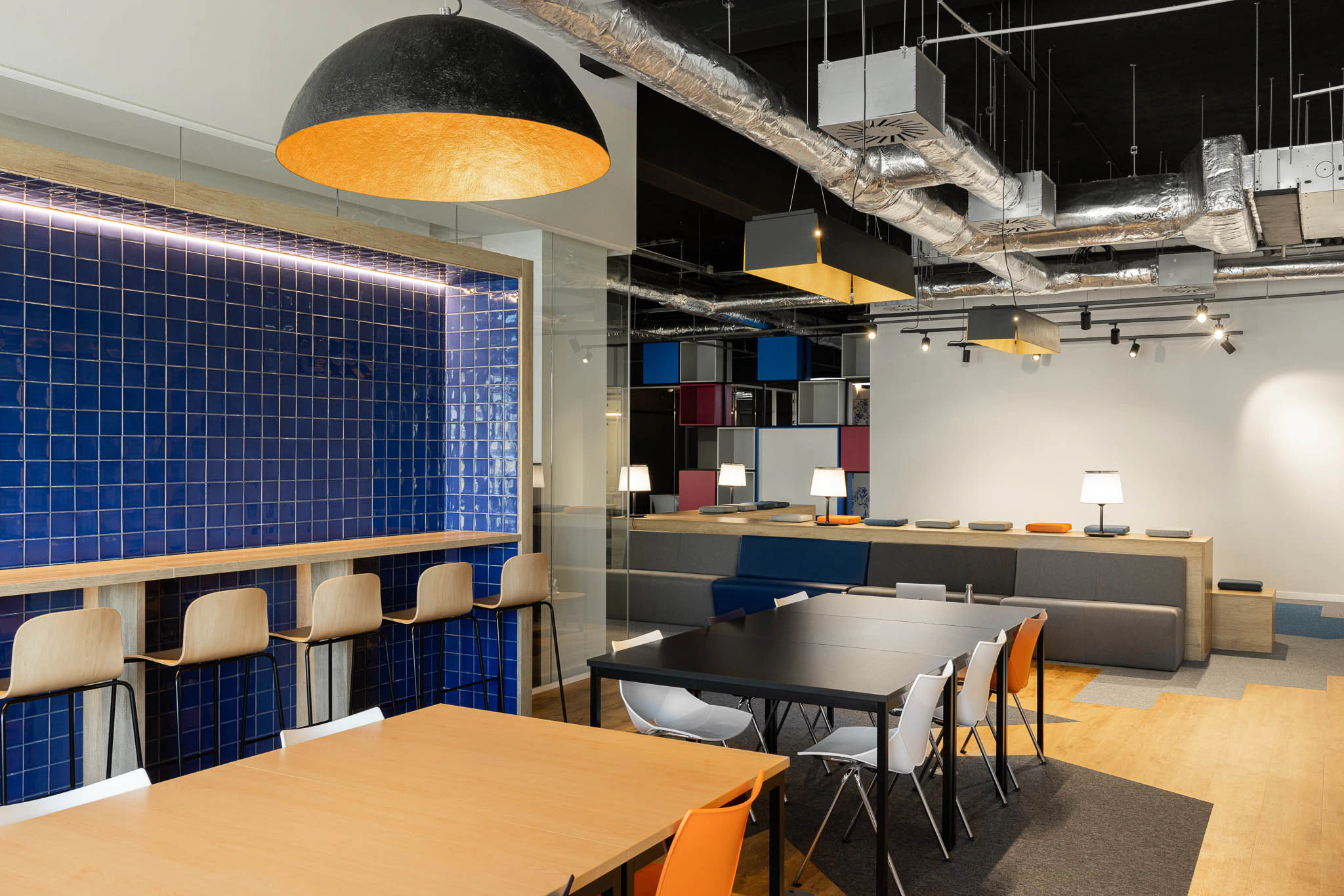 Zona de refeições com balcão em azulejo azul, cadeiras de madeira e iluminação suspensa. — Bold by Devoteam: Escritório Porto arquitetura Inception Architects Studio em Porto