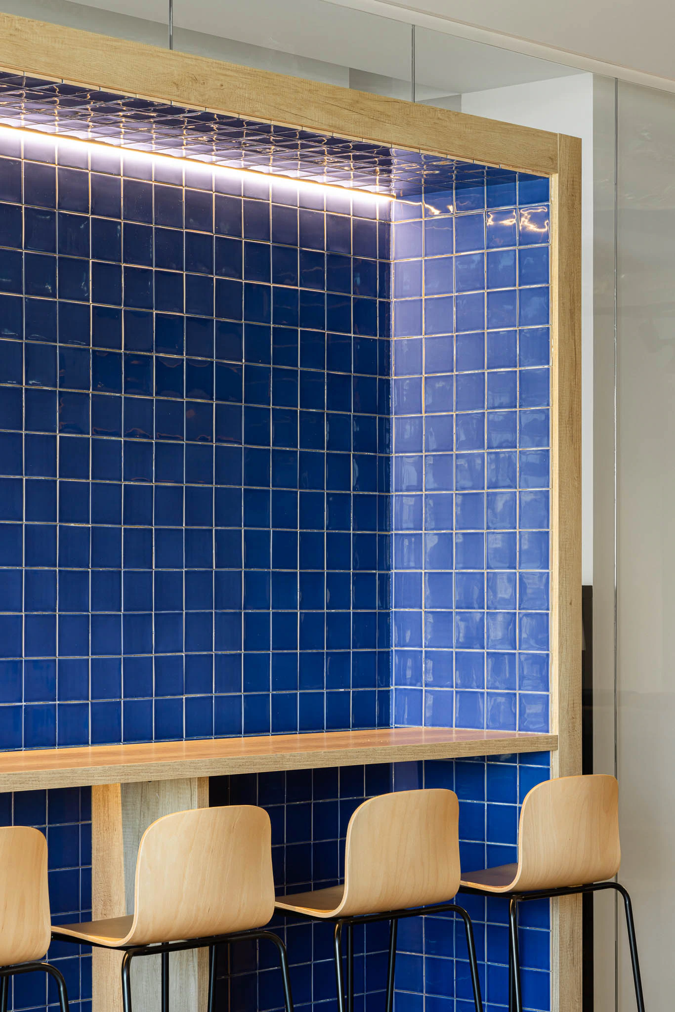 Detalhe do balcão em azulejo azul com cadeiras de madeira e iluminação embutida. — Bold by Devoteam: Escritório Porto arquitetura Inception Architects Studio em Porto