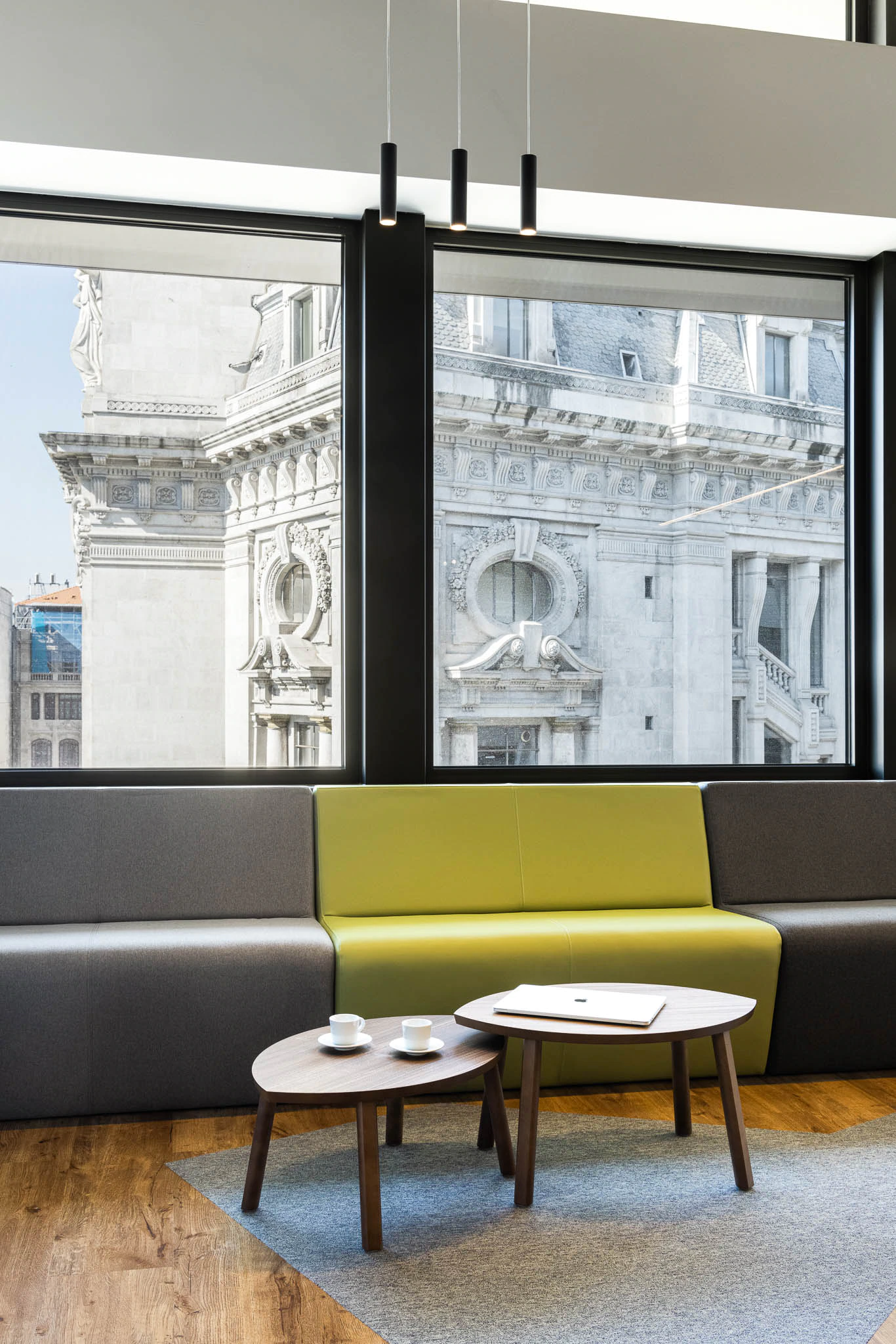 Zona de descanso com sofá modular colorido, mesas de apoio e vista para um edifício histórico. — Bold by Devoteam: Escritório Porto arquitetura Inception Architects Studio em Porto