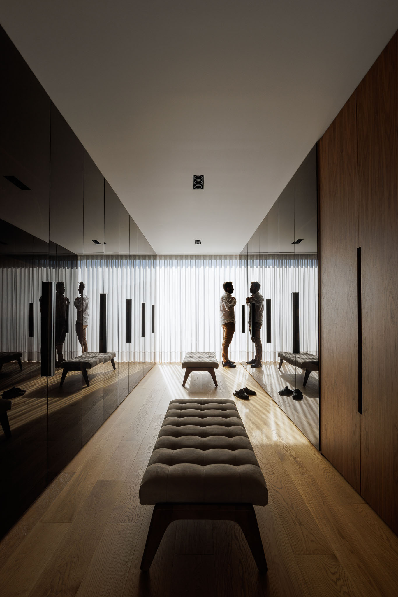Closet: Closet com armários espelhados e de madeira, banco almofadado e pavimento em madeira. — Casa D arquitetura L2C Arquitetura em Braga