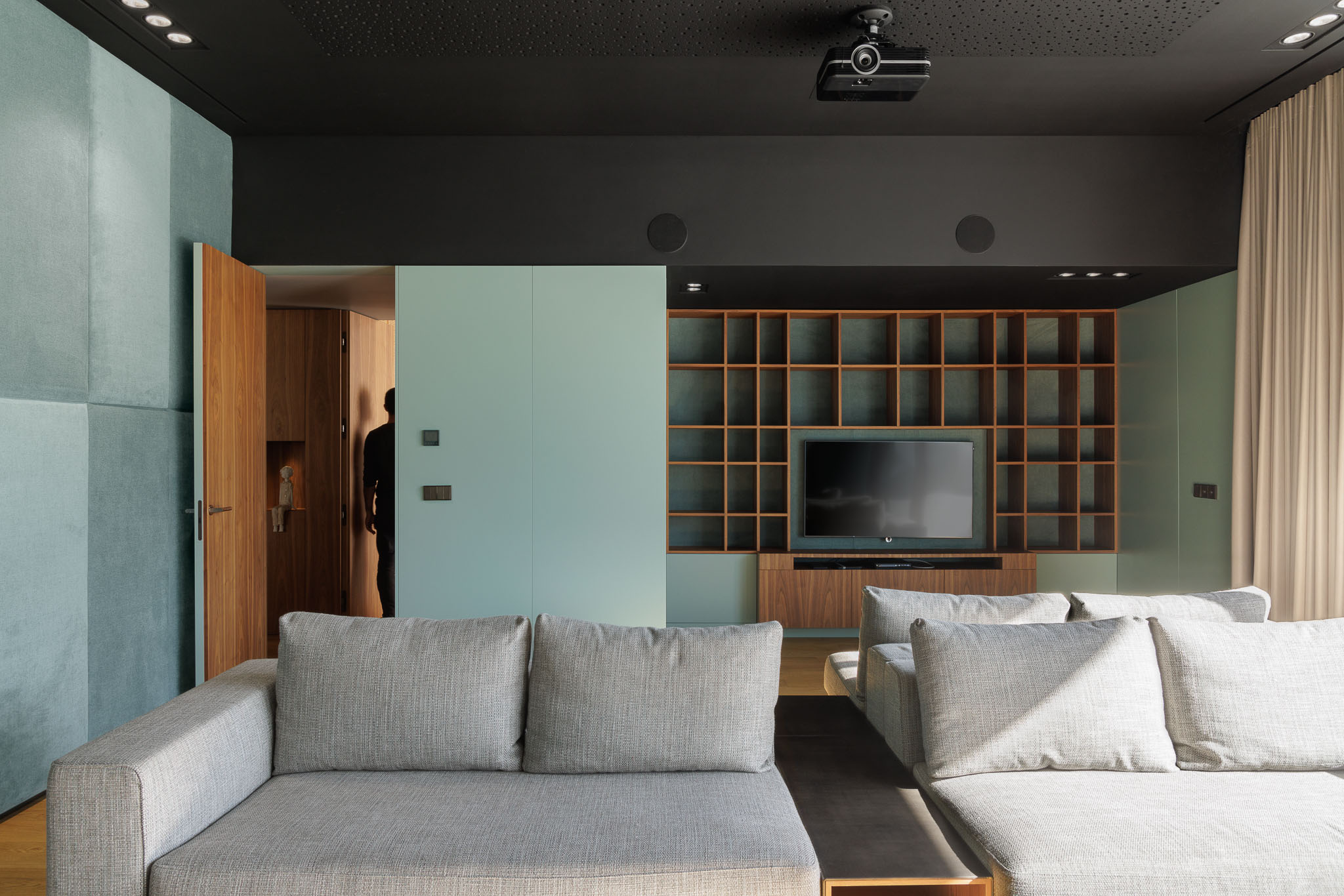 Sala de estar: Sala de estar com sofás cinzentos, parede azul clara e estante em madeira escura. — Casa D arquitetura L2C Arquitetura em Braga