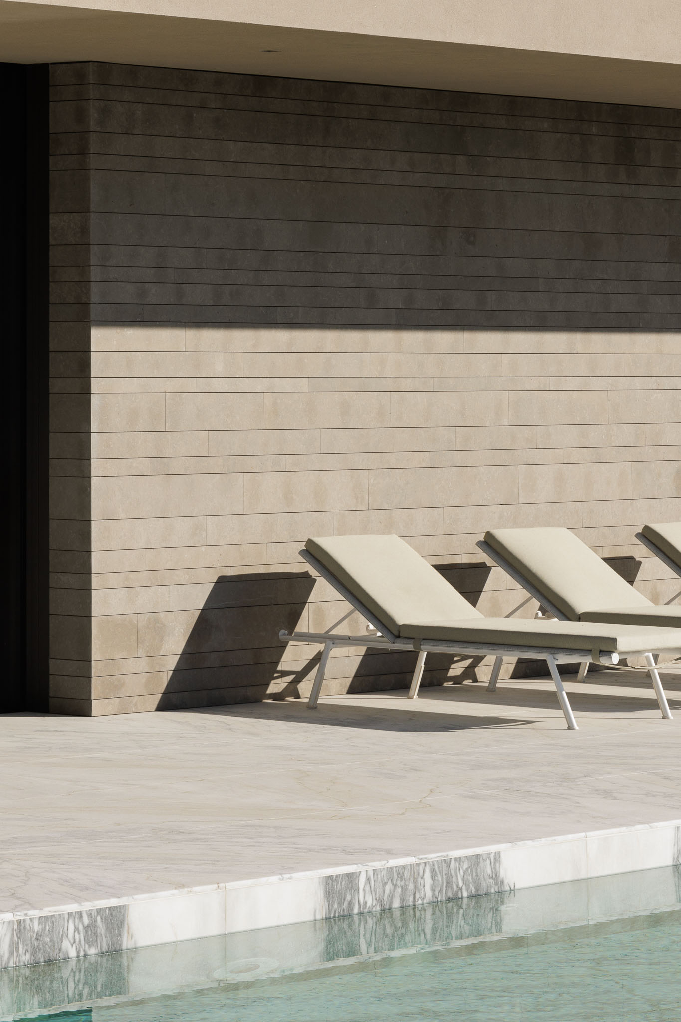 Piscina: Espreguiçadeiras junto à piscina com borda em mármore e parede revestida a pedra. — Casa D arquitetura L2C Arquitetura em Braga