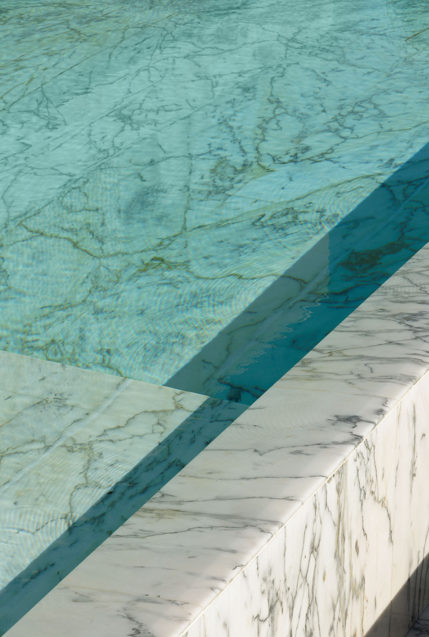Piscina: Detalhe da borda em mármore da piscina com água cristalina. — Casa D arquitetura L2C Arquitetura em Braga