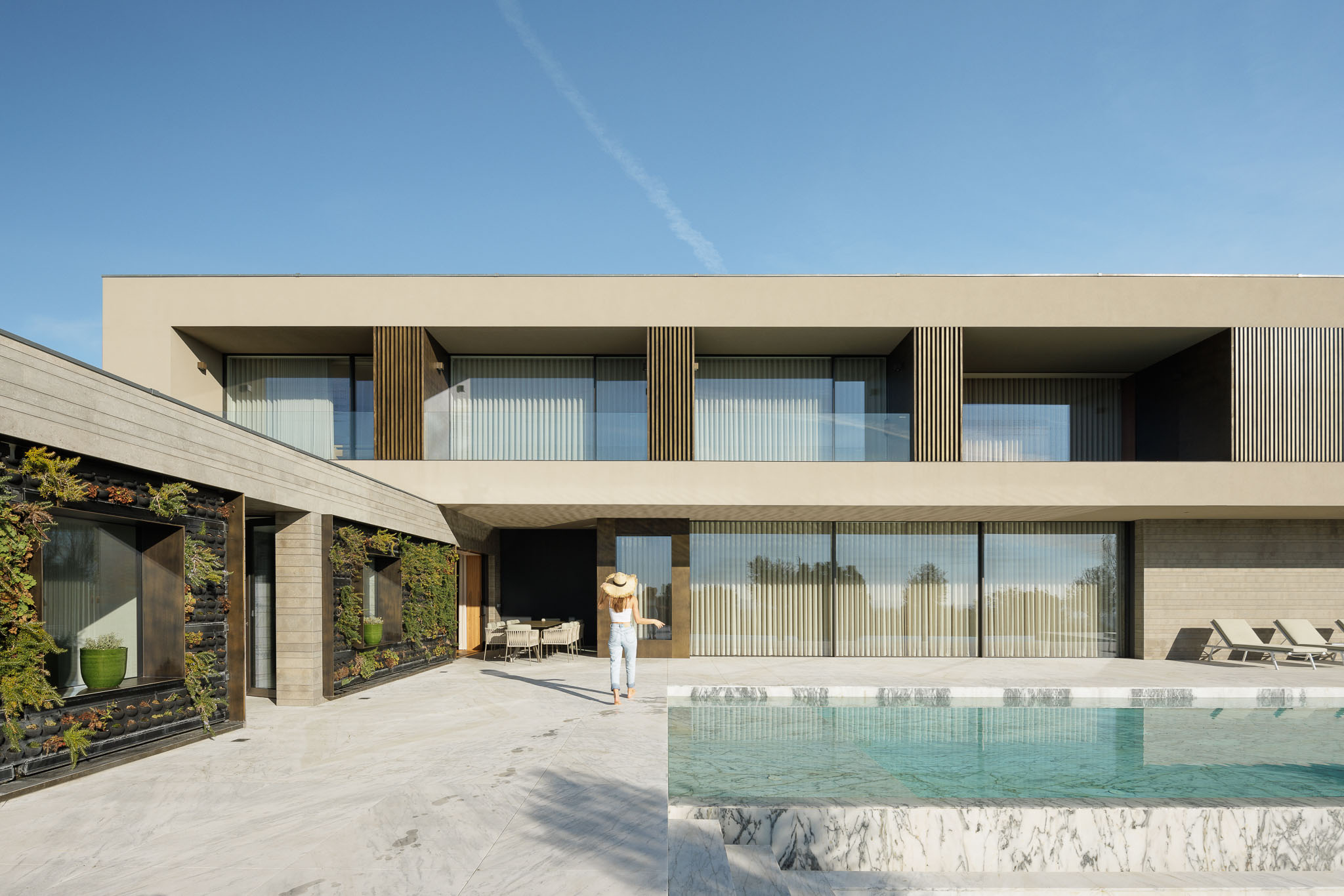 Piscina: Mulher deitada junto à piscina com pavimento em mármore e chapéu de palha. — Casa D arquitetura L2C Arquitetura em Braga
